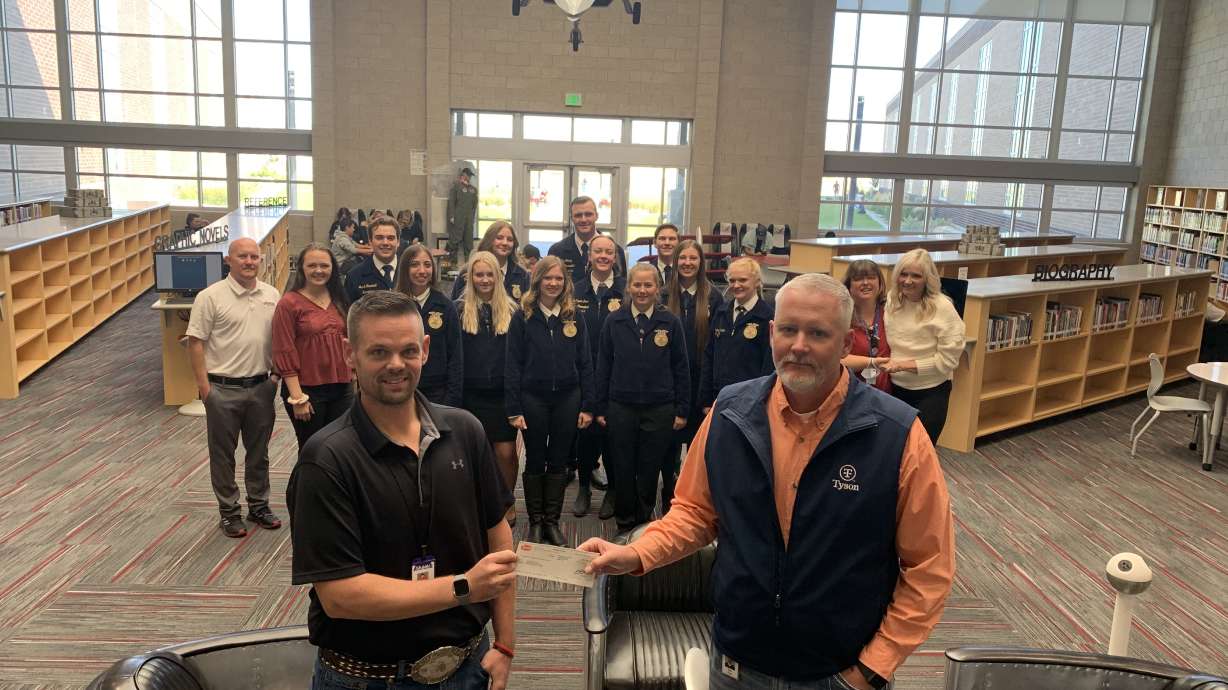 Tom Sharp, complex manager at Eagle Mountain's Tyson Foods facility, hands Cody Gull, agriculture teacher at Cedar Valley High School, a donation to help them build a barn so the students can have hands-on experience with animals on Friday.