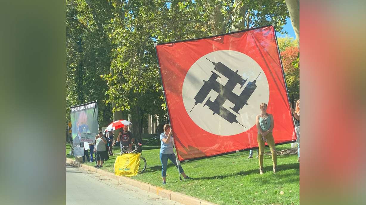 Anti-vaccine demonstrators displayed a large banner fashioned after a Nazi flag and featuring a swastika made out of vaccine syringes during a protest at the Governor's Mansion in Salt Lake City on Sunday.