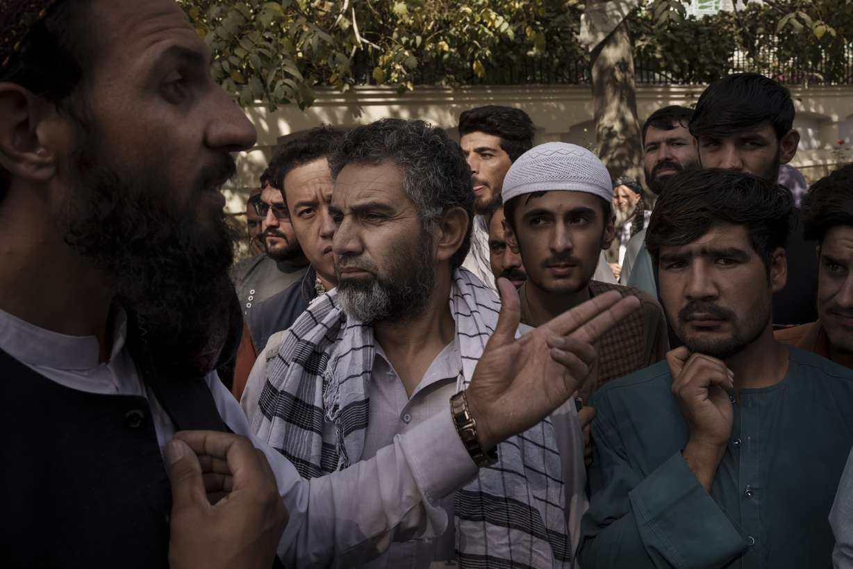 A member of the Taliban, left, talks to Afghans gathering outside a government passport office recently re-opened after Taliban announced they would be issuing a backlog of applications approved by the previous administration in Kabul, Afghanistan, Wednesday.