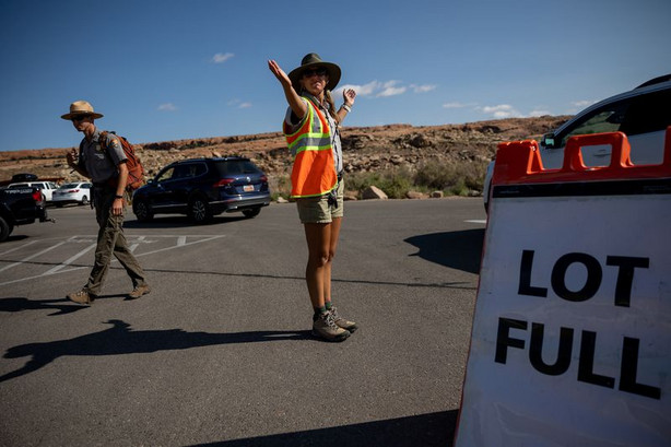 A visitor services assistant directs traffic around the full Wolfe Ranch parking lot, which serves as the starting point for the popular hike to Delicate Arch, in Arches National Park on Sunday, Sept. 19.