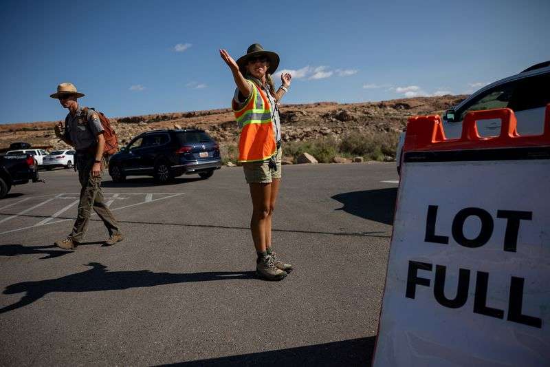A visitor services assistant directs traffic around the full Wolfe Ranch parking lot, which serves as the starting point for the popular hike to Delicate Arch, in Arches National Park on Sunday, Sept. 19.