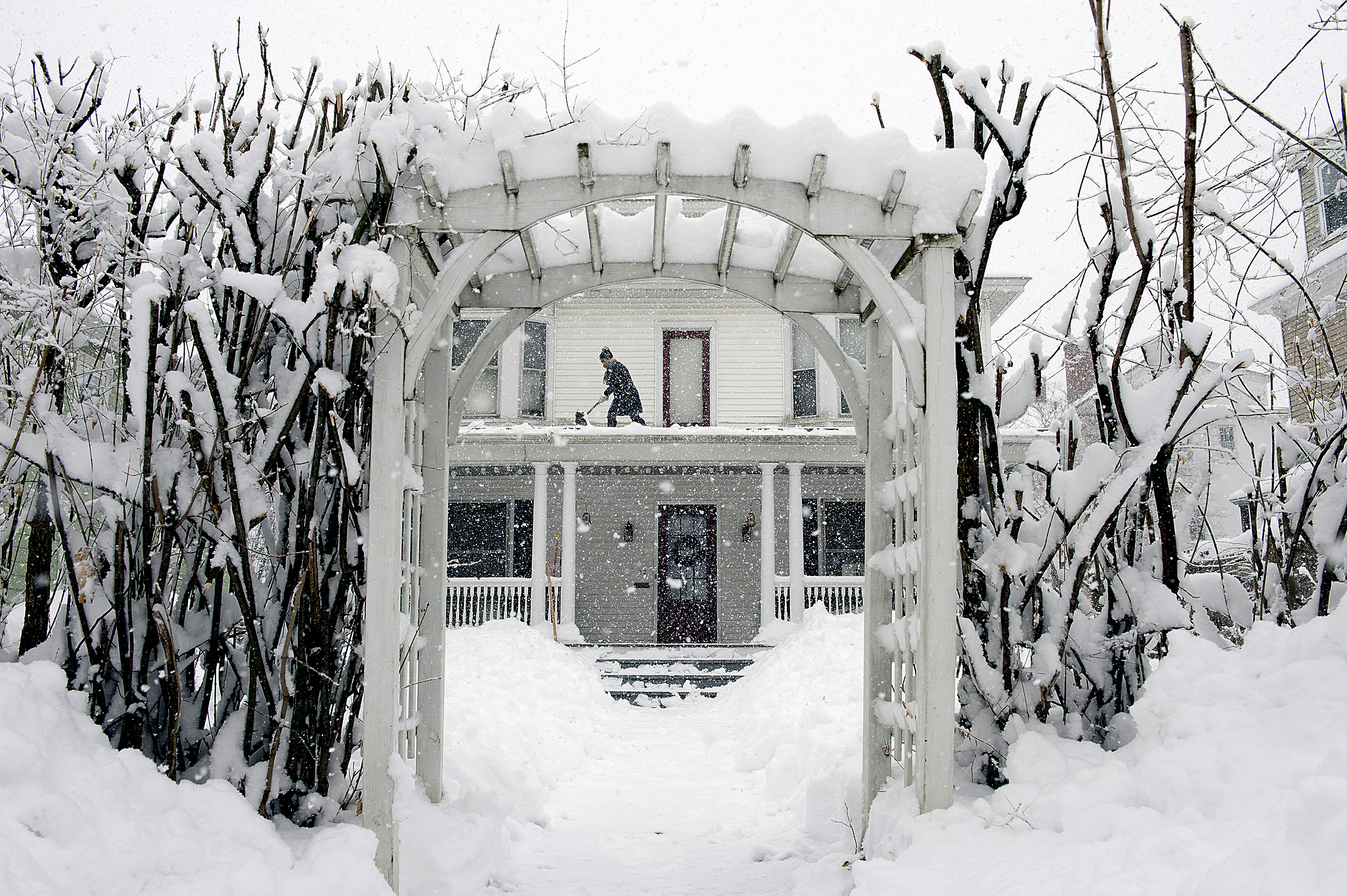 Amber Cox shovels snow from the porch roof at her home in Auburn, Maine, on March 8, 2018. With prices surging worldwide for heating oil, natural gas and other fuels, the U.S. government said Wednesday, Oct. 13, 2021 it expects households to see jumps of up to 54% for their heating bills compared to last winter.