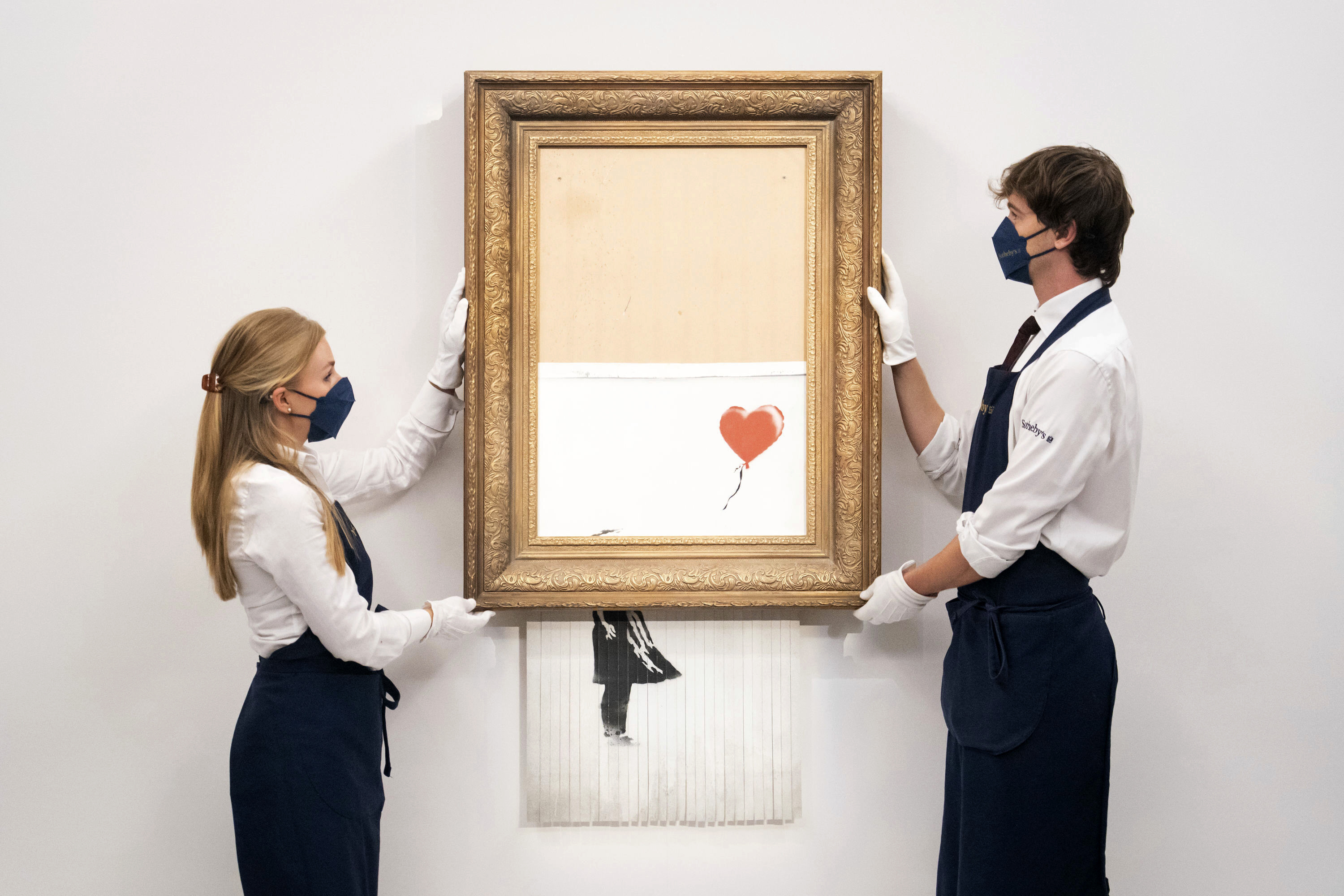 Art handlers at Sotheby's auction house hold Banksy's 'Love is in the Bin', before it returns to auction at Sotheby's, London, on Sept. 3. The work by British street artist Banksy that sensationally self-shredded just after it sold for $1.4 million made several times that price, $25.4 million, at an auction on Thursday.