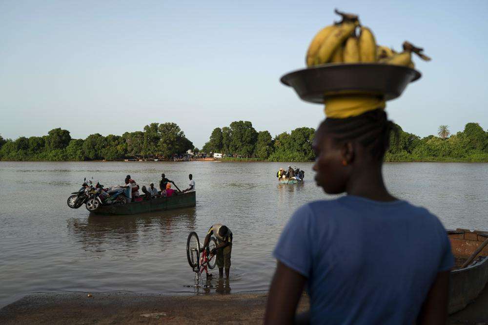 Carrying bananas for sale, a woman waits for the boat to cross the Gambia river in Bansang, Gambia, Tuesday, Sept. 28, 2021. As health officials in Gambia and across Africa urge women to be vaccinated, they've confronted hesitancy among those of childbearing age. Although data on gender breakdown of vaccine distribution are lacking globally, experts see a growing number of women in Africa's poorest countries consistently missing out on vaccines.
