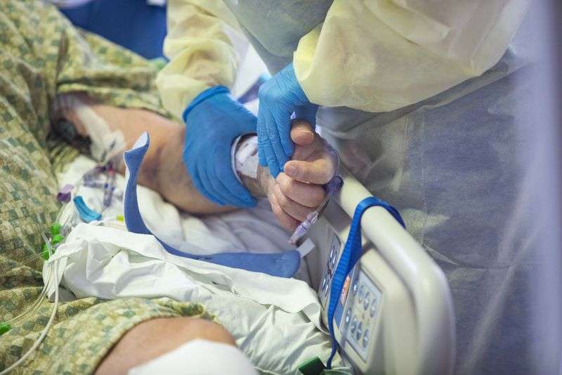 A registered nurse holds the hand
of a COVID-19 patient in the intensive care unit at St. Luke’s Boise Medical Center in Boise on Aug. 31.