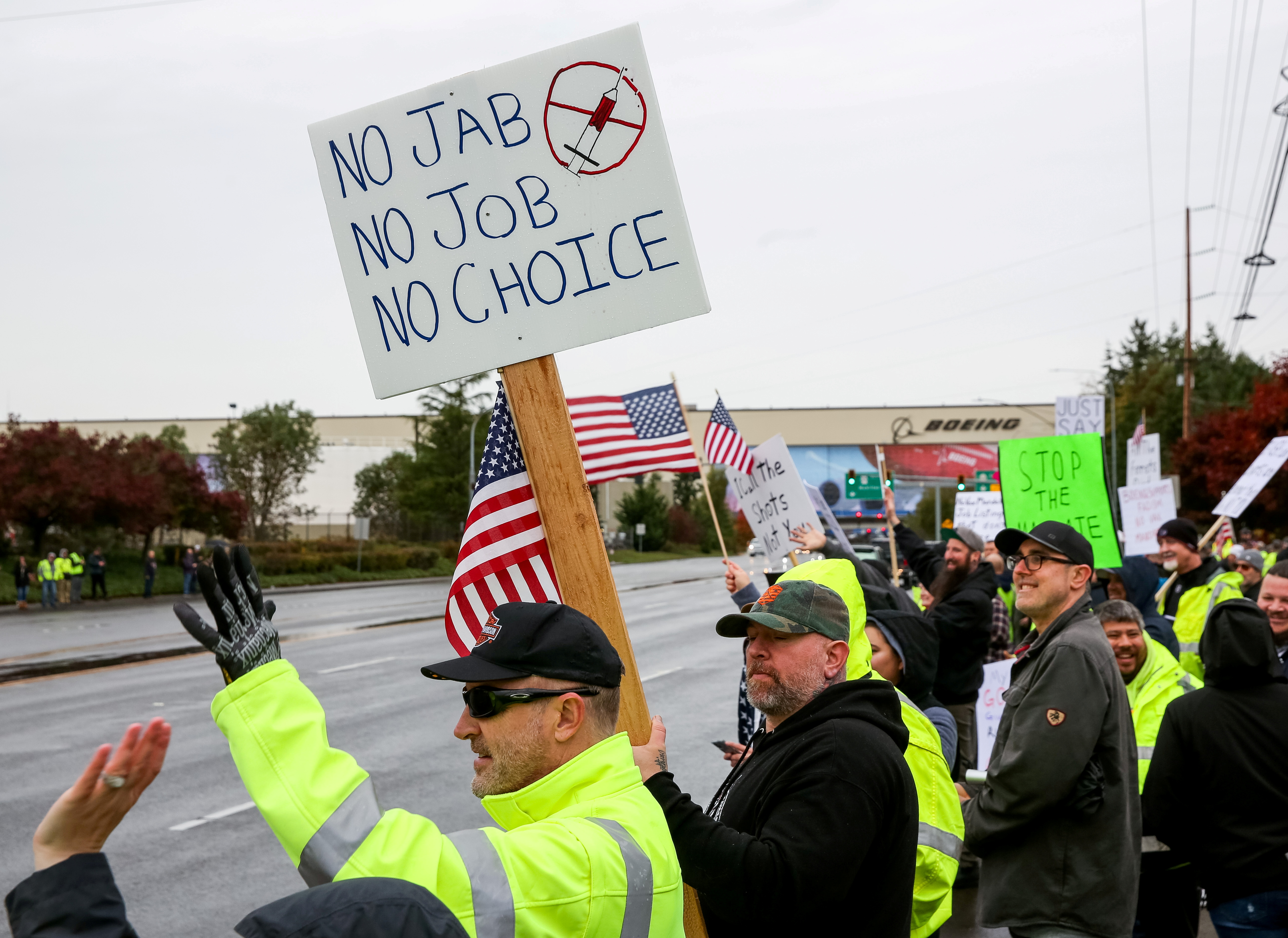 Boeing employees and others line the street with signs and American flags as they protest the company's coronavirus disease vaccine mandate, outside the Boeing facility in Everett, Washington, Oct. 15. Thousands of unvaccinated workers across the United States are facing potential job losses as a growing number of states, cities and private companies start to enforce mandates for inoculation against COVID-19.