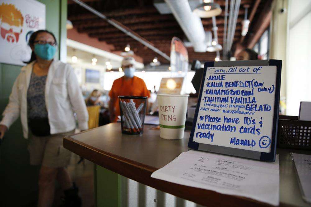 Customers walk past a sign reminding people to have their vaccination cards ready at Highway Inn restaurant in Honolulu on Monday. To comply with local mandates, the restaurant requires all indoor diners to show proof of vaccination or have a recent negative test result before being seated.