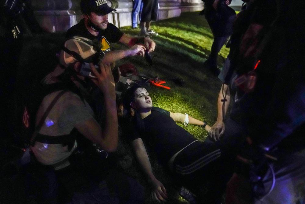 In this Aug. 25, 2020 photo, Gaige Grosskreutz, top, tends to an injured protester during clashes with police outside the Kenosha County Courthouse in Kenosha, Wis. Grosskreutz, who was allegedly shot in the arm by Kyle Rittenhouse during street protests in Kenosha last year, has filed a federal lawsuit that accuses police of enabling the violence by allowing an armed militia to roam freely during the demonstration.