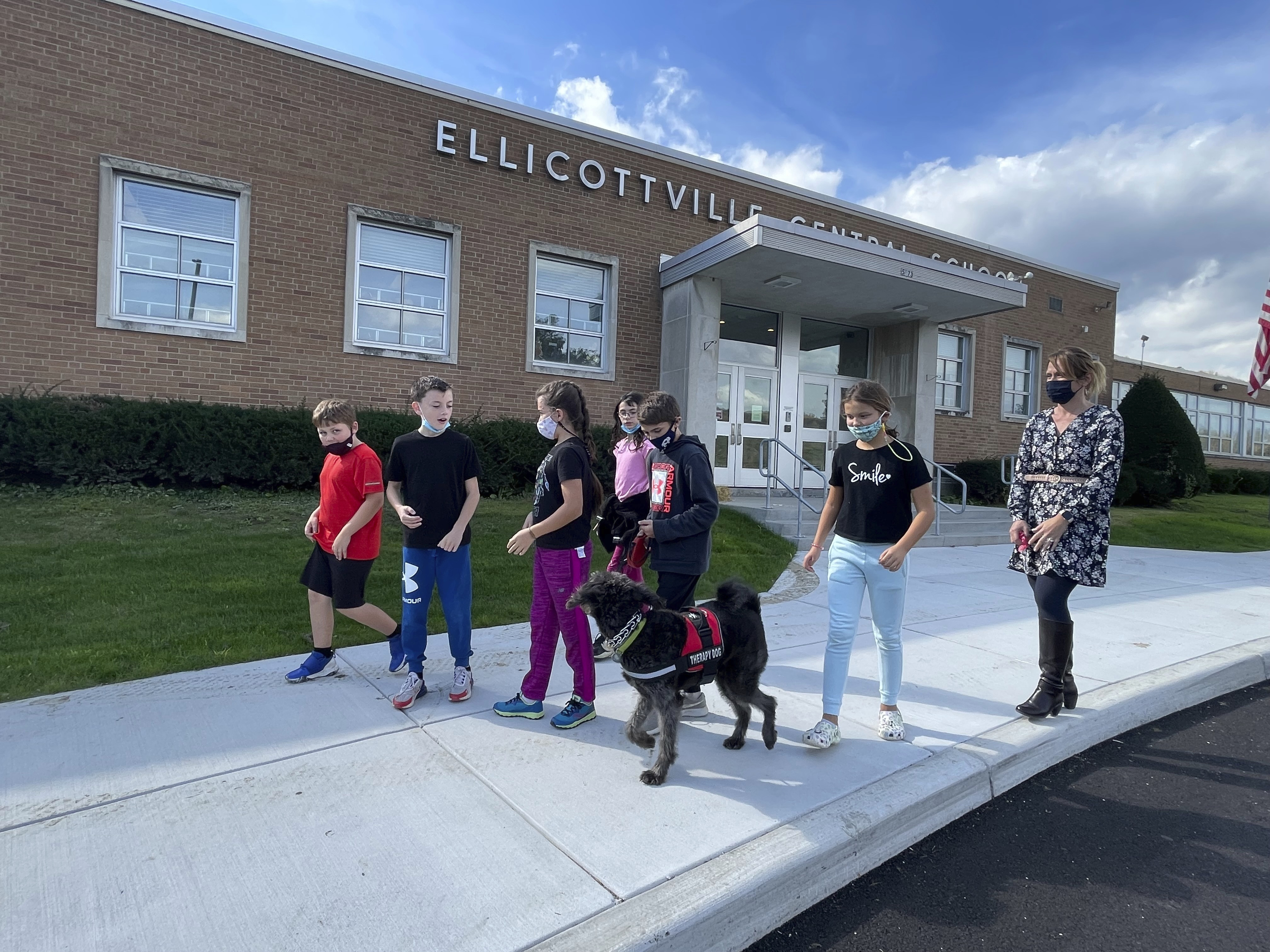 Students from Ellicottville Central Schools in Ellicottville, N.Y., walk therapy dog Toby outside the rural school on Oct. 21 accompanied by the dog's owner, elementary school principal Maren Bush, right. Bush lets students walk and visit with Toby as part of the district's efforts to improve students' mental well-being, a focus of schools nationwide following pandemic disruptions. 