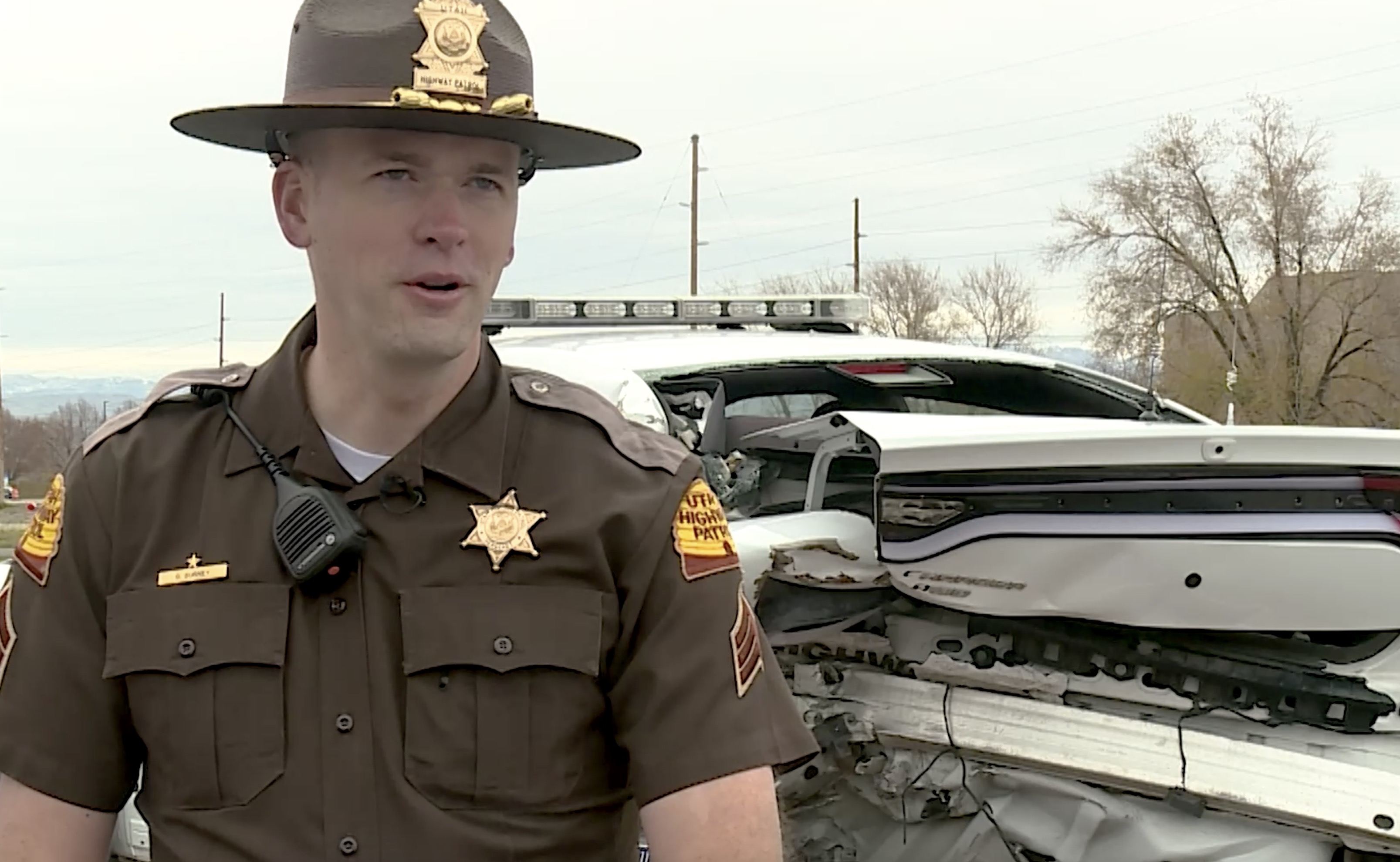Utah Highway Patrol Sgt. Devyn Gurney speaks with members of the media on Thursday in front of his mangled patrol car. Gurney was struck by it in 2017 after it was rear-ended while he was conducting a traffic stop.