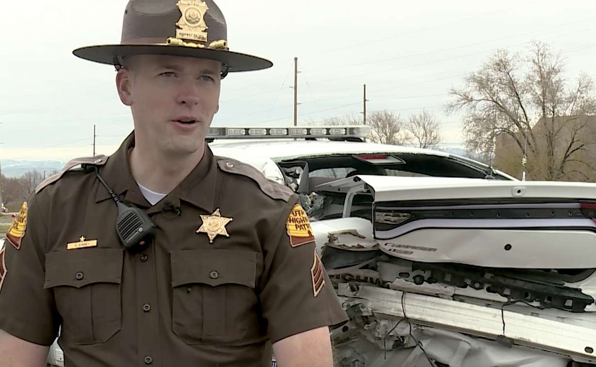 Utah Highway Patrol Sgt. Devyn Gurney speaks with members of the media on Thursday in front of his mangled patrol car. Gurney was struck by it in 2017 after it was rear-ended while he was conducting a traffic stop.