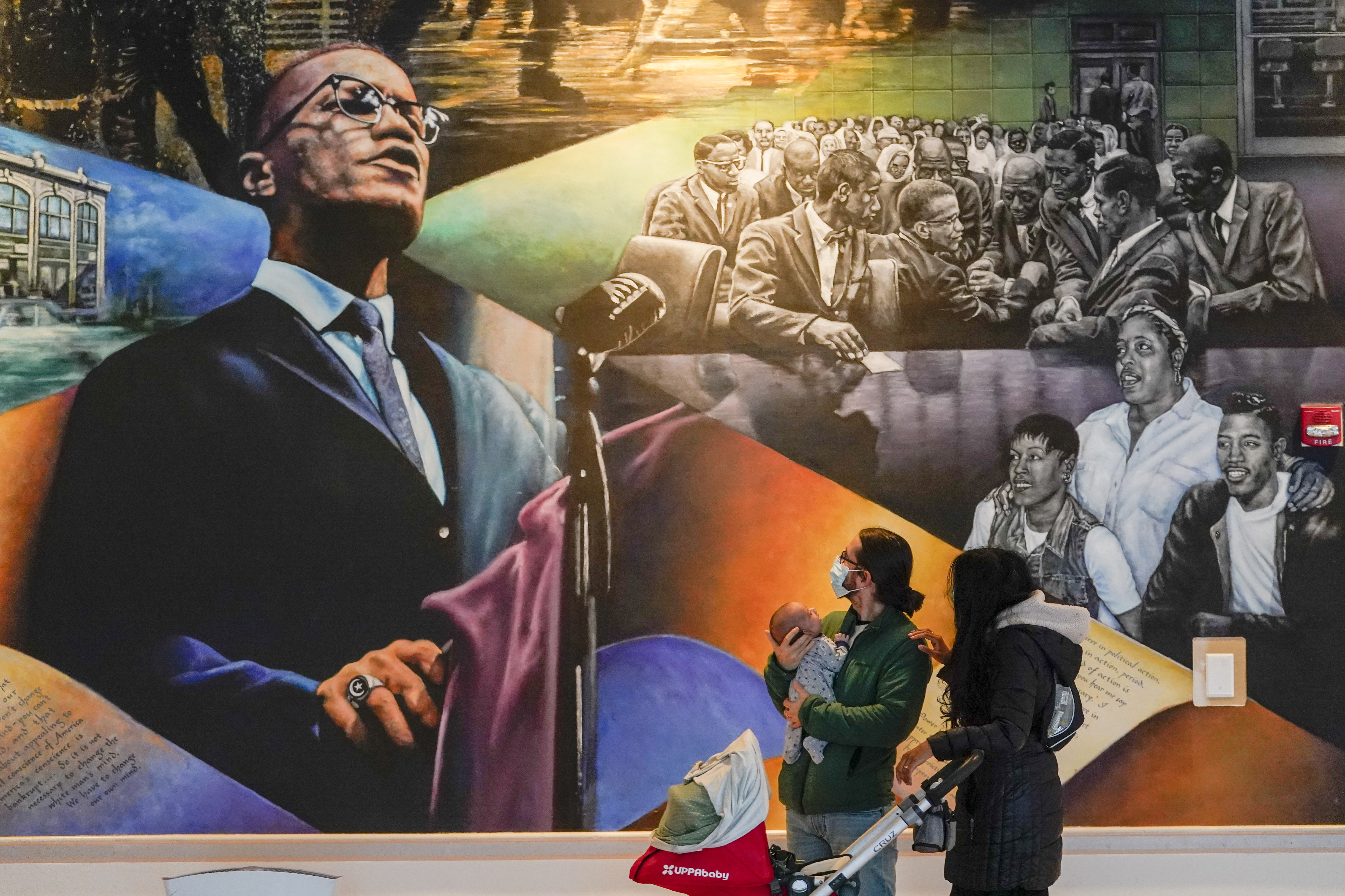 Aaron Page, left, and Kalyani Thampi inspect the mural by Daniel Galvez titled "Homage to Malcolm X" with their 6 week old son Sury Thampi-Paige at the Malcolm X & Dr. Betty Shabazz Memorial and Educational Center, formerly the Audubon Ballroom, Wednesday, in New York. Two of the three men convicted in the assassination of Malcolm X are set to be cleared Thursday, after insisting on their innocence since the 1965 killing.