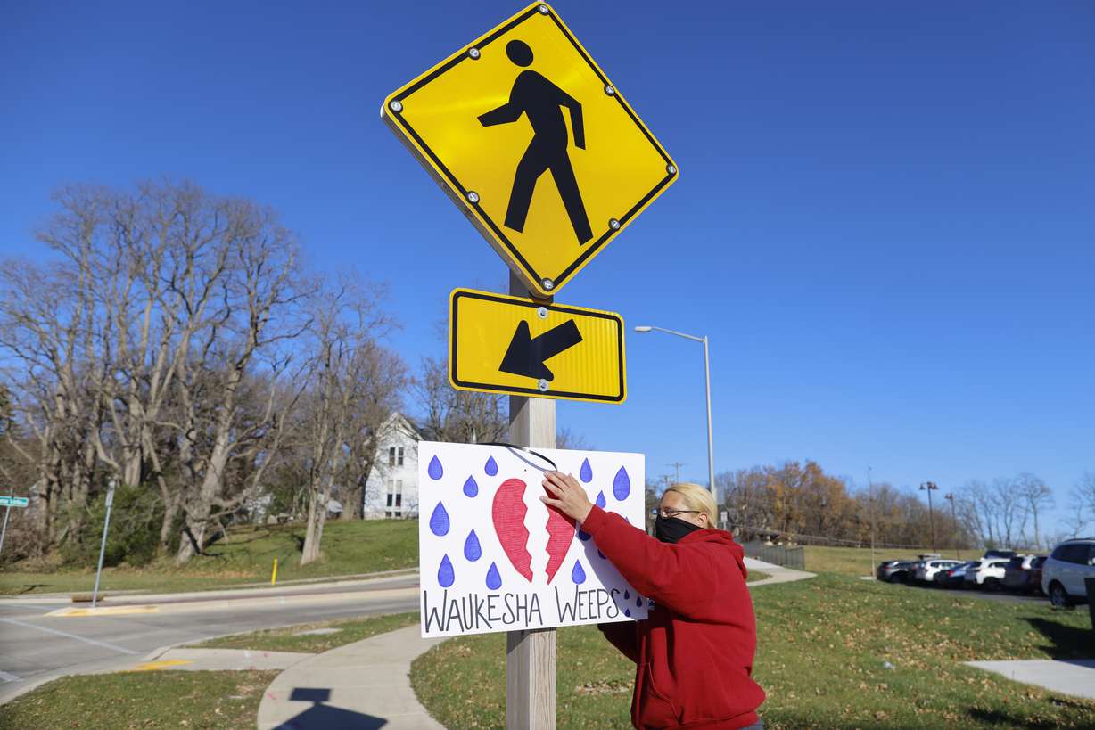 A woman puts up a sign outside City Hall in Waukesha, Wis., on Monday after an SUV plowed into a Sunday Christmas parade, killing several and injuring dozens of others.
