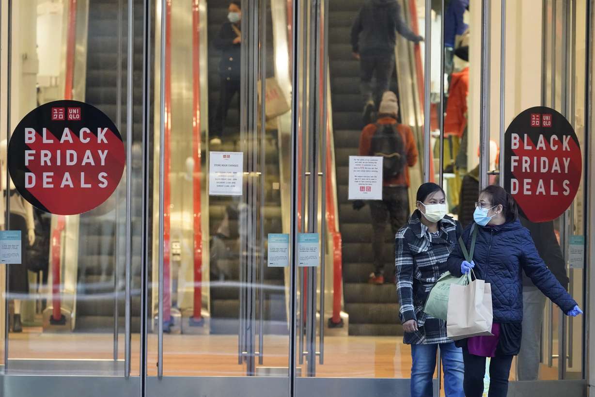 Black Friday shoppers wear face masks and gloves during the coronavirus pandemic as they leave the Uniqlo store along Fifth Avenue, Friday, Nov. 27, 2020, in New York.