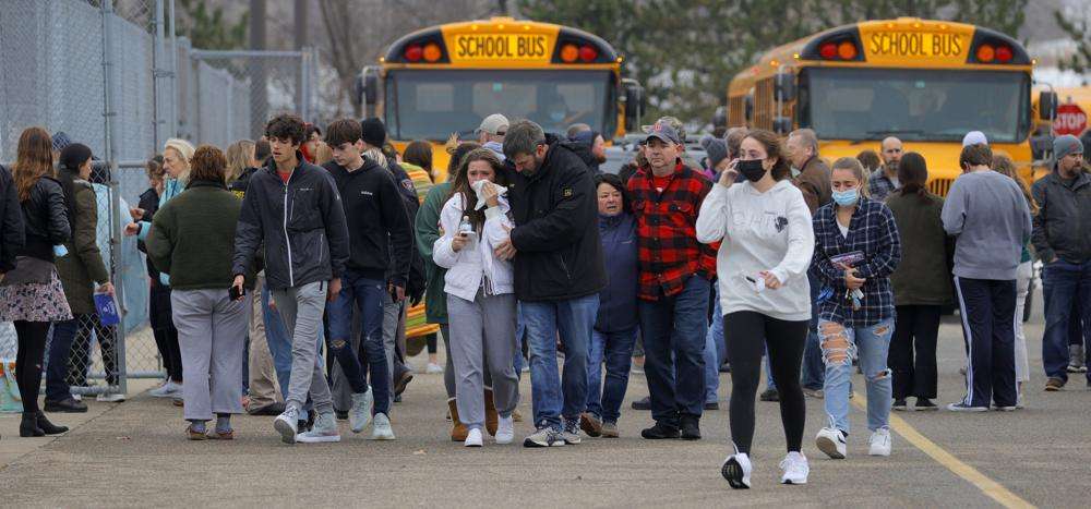 Parents walk away with their kids from the Meijer's parking lot, where many students gathered following an active shooter situation at Oxford High School, Tuesday, in Oxford, Mich. Police took a suspected shooter into custody and there were multiple victims, the Oakland County Sheriff's office said.