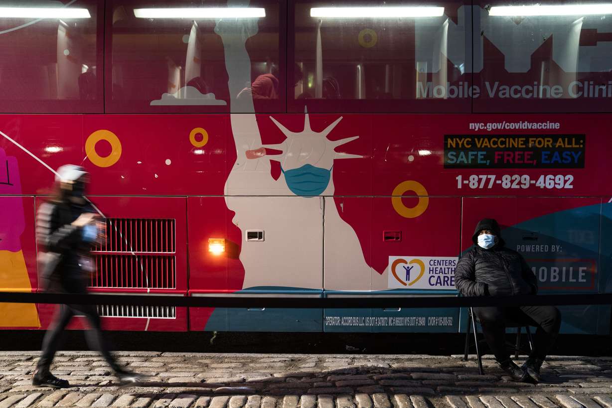 A mobile COVID-19 vaccination and booster shot site operates out of a bus on 59th Street south of Central Park as patients wait on the sidewalk on Thursday in New York. Health officials say multiple cases of the omicron coronavirus variant have been detected in New York, including a man who attended an anime convention in Manhattan in late November and tested positive for the variant when he returned home to Minnesota.