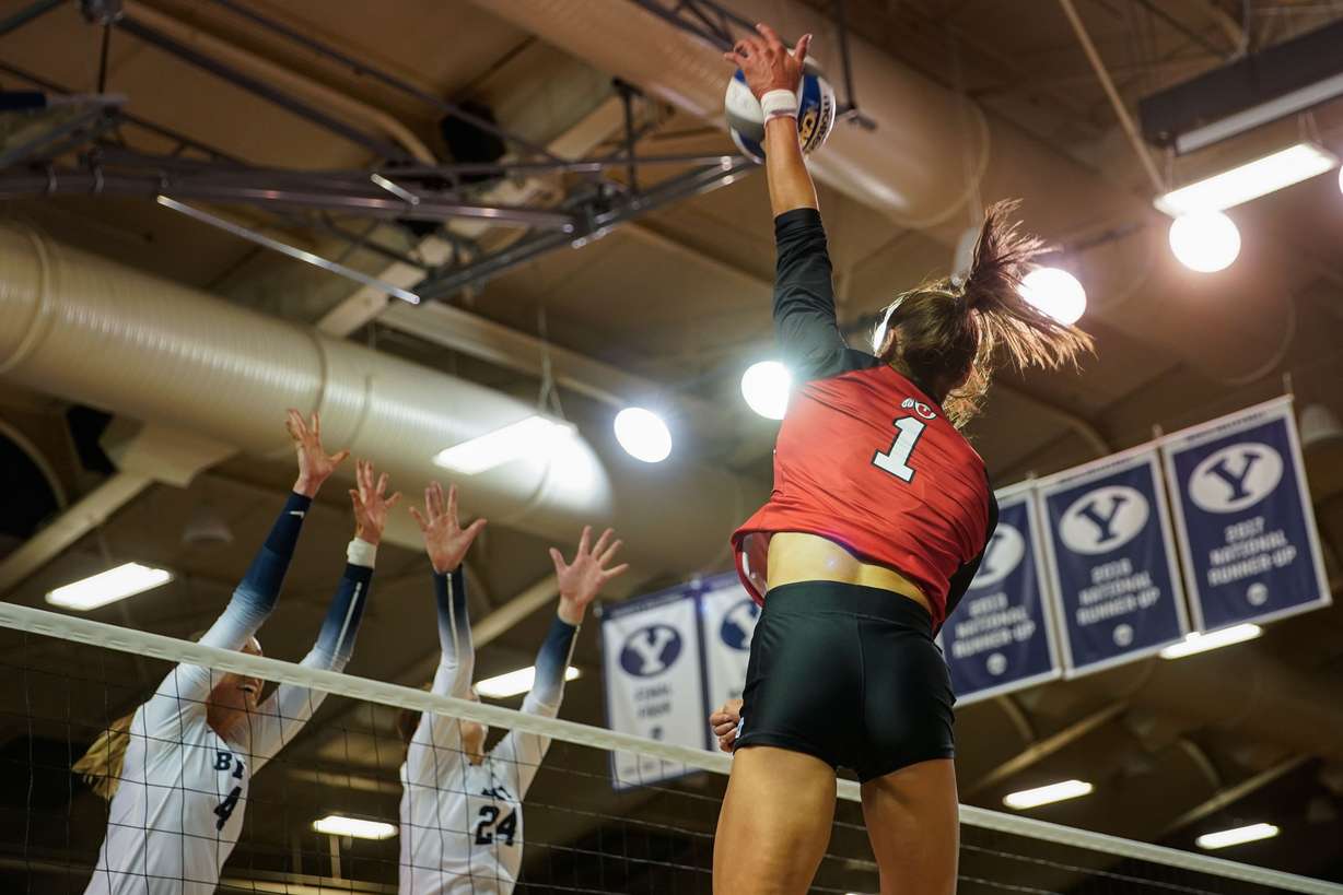 Utah’s Dani Drews (1) hits the ball as BYU’s Kenzie Koerber, left and Kennedy Eschenberg jumps to block in an NCAA volleyball game at Smith Fieldhouse in Provo on Saturday, Dec. 4, 2021.