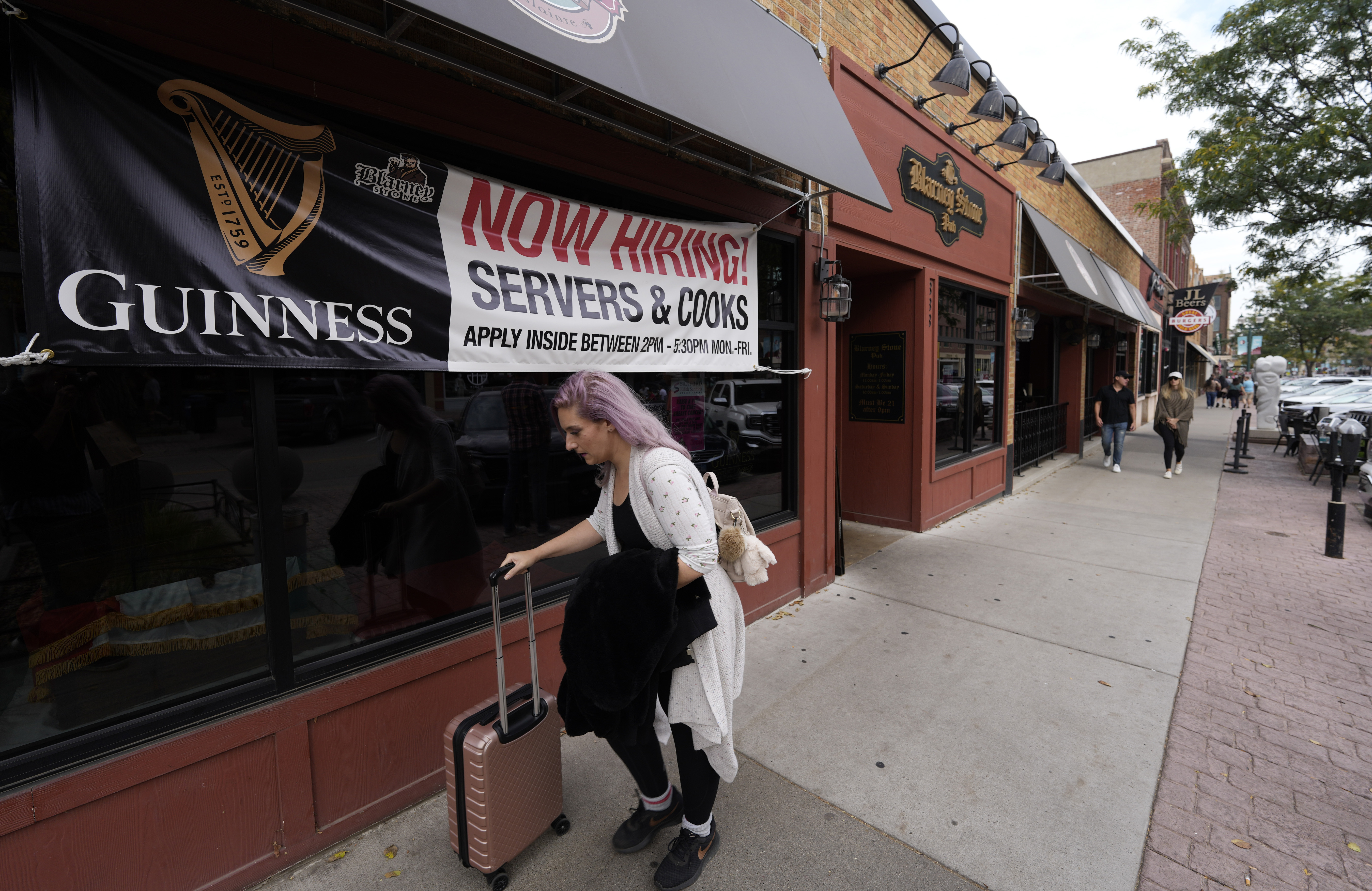 A traveler wheels her baggage past a now hiring sign outside a bar and restaurant Oct. 9, in Sioux Falls, S.D. The number of Americans applying for unemployment benefits plunged last week to the lowest level in 52 years,