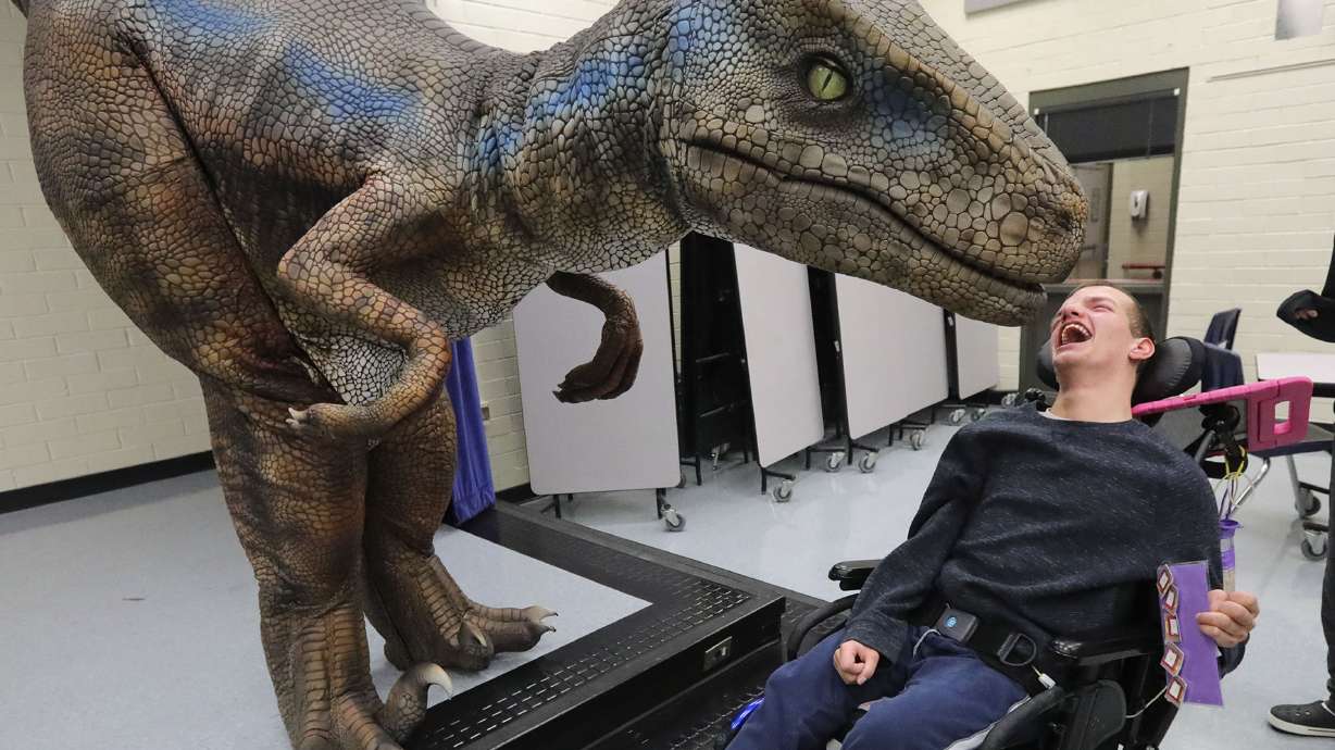 Nathan Curtis, Jordan Valley School post high school student, reacts as a Dino and Dragon Stroll raptor approaches him at Jordan Valley School in Midvale on Thursday, Dec. 9. Tomas Lara is inside the Raptor suit.