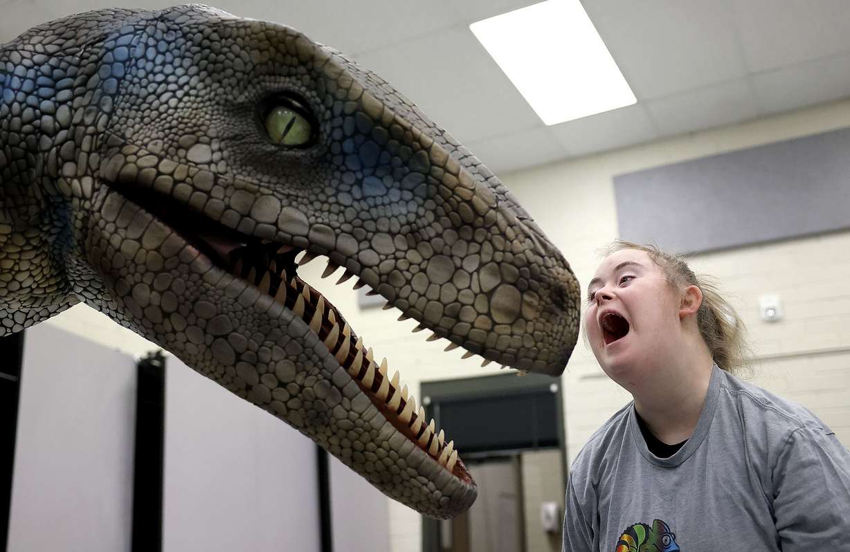 Monet Heath, a Jordan Valley School first year post high school student, roars at a Dino and Dragon Stroll raptor at Jordan Valley School in Midvale on Thursday, Dec. 9. Tomas Lara is inside the Raptor suit.