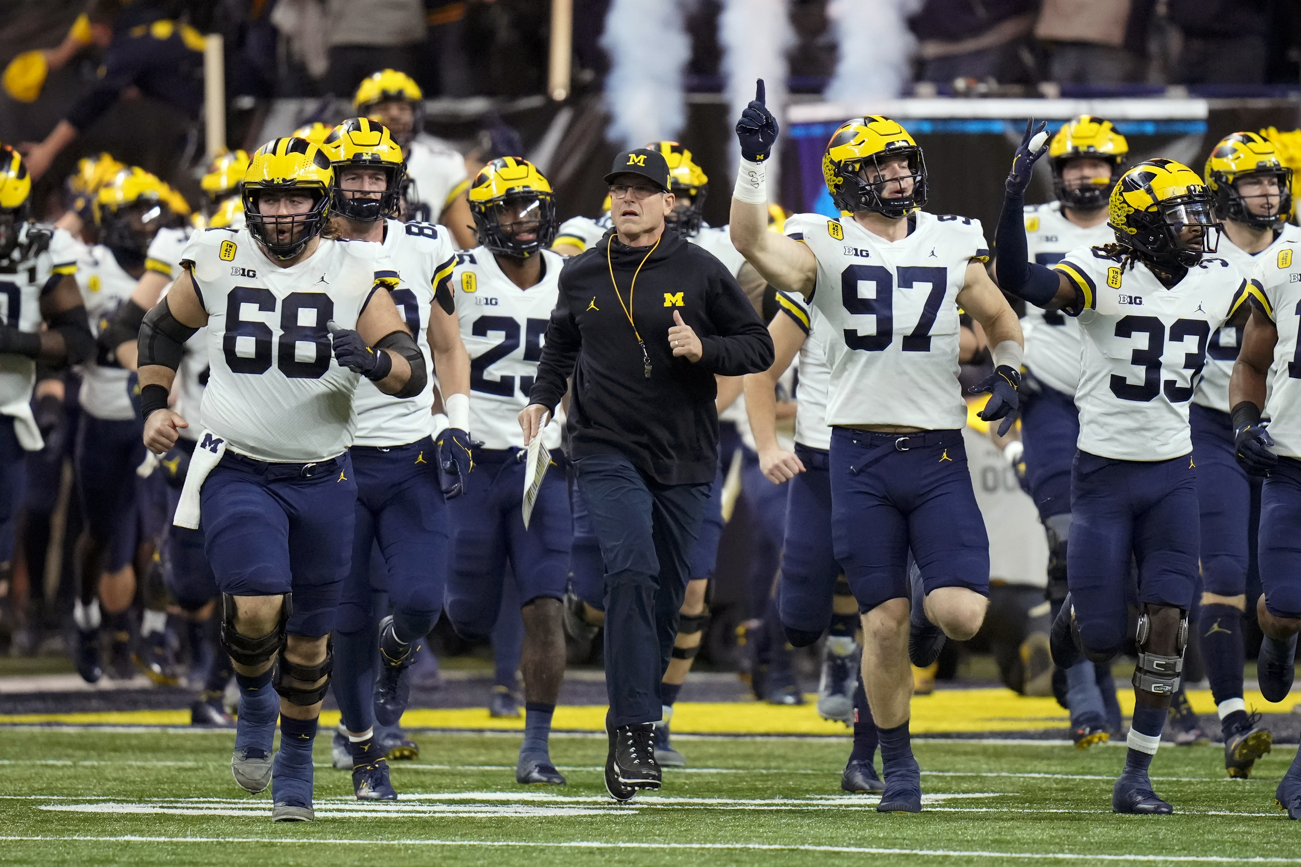Michigan head coach Jim Harbaugh runs onto the field with his team before the Big Ten championship NCAA college football game against Iowa, Saturday, Dec. 4, in Indianapolis. 