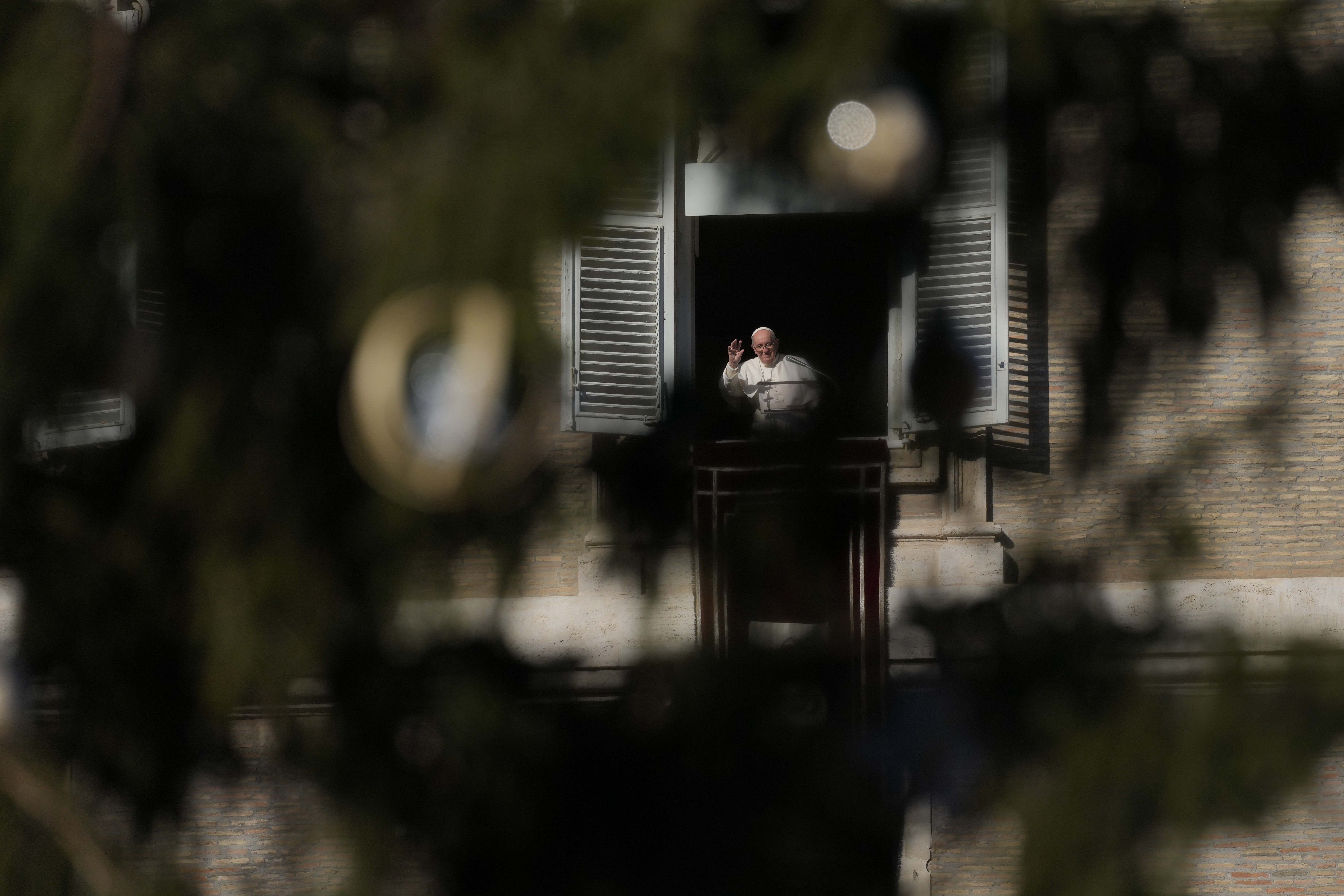 Pope Francis, framed by the Vatican Christmas tree, salutes pilgrims and faithful during the Angelus noon prayer from the window of his studio overlooking St.Peter's Square, at the Vatican, Sunday. 