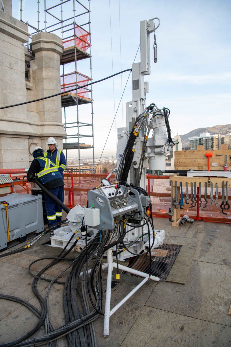 Workers use one of two drills positioned on the roof of
the Salt Lake Temple to drill inside tower and wall columns in Salt
Lake City, in December 2021. When the drilling is done, crews
will insert post-tension cables that will be anchored into the
foundation 80 feet below.