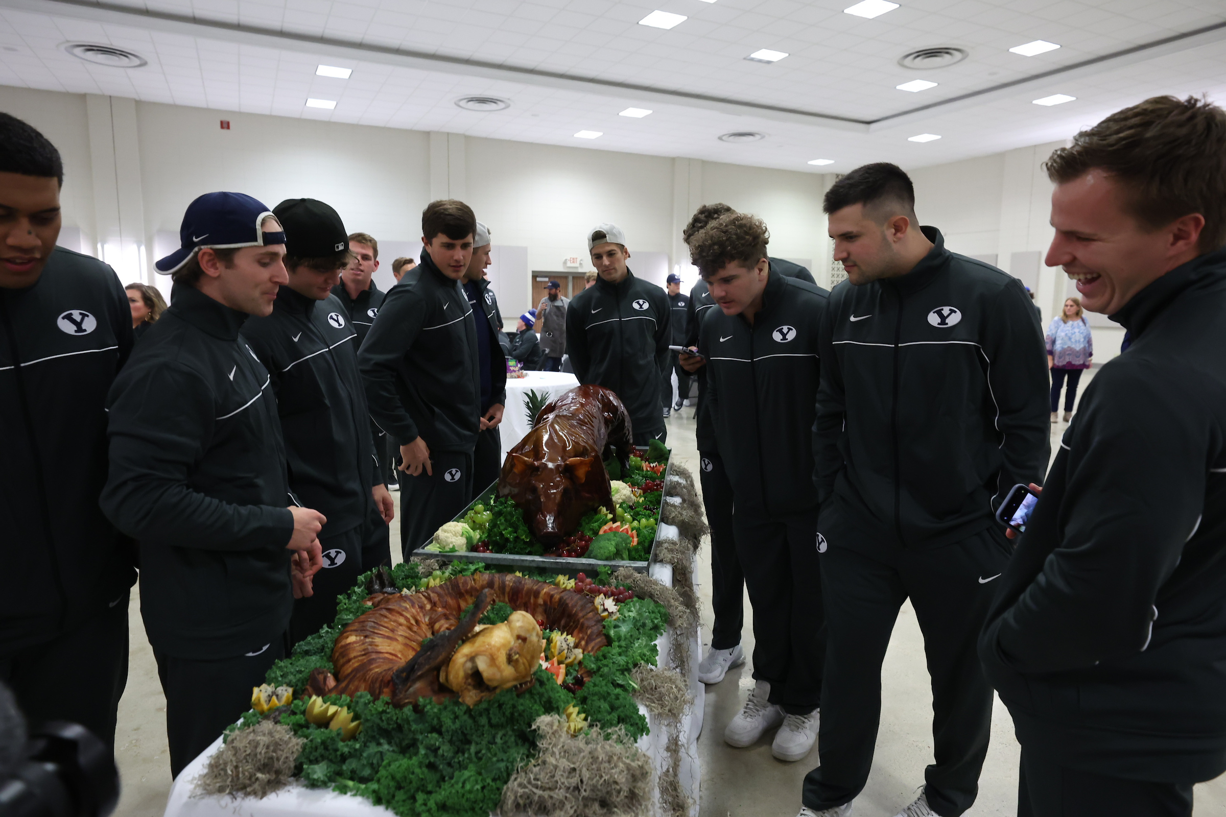 BYU football players crowd around a roast pig and bacon-wrapped alligator during an Independence Bowl welcome dinner, Tuesday, Dec. 14, 2021 in Shreveport, Louisiana.