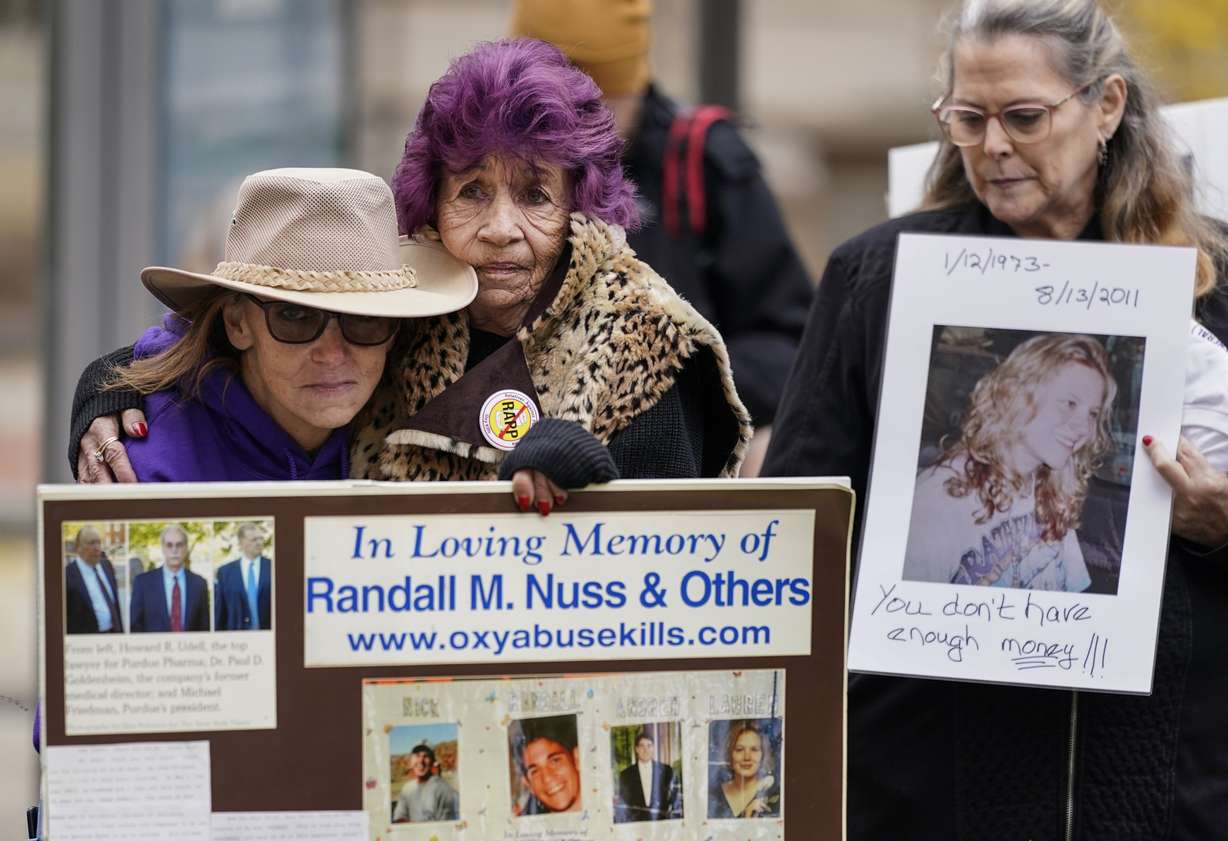 Ellen Isaacs, left, and Lee Nuss, center, both from Florida, hold each other and a sing of remembrance of Randall M. Nuss, Lee's husband, during a protest with other advocates for opioid victims outside the Department of Justice, Friday, Dec. 3, 2021, in Washington. A federal judge has rejected OxyContin maker Purdue Pharma’s sweeping deal to settle thousands of lawsuits over the toll of opioids. U.S. District Court Judge Colleen McMahon in New York found flaws in the way the bankruptcy settlement protects members of the Sackler family who own the company from lawsuits.