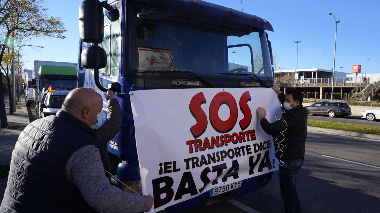 Truckers tie a banner reading "SOS Transport. That's enough" to a truck before driving slowly during a protest though Madrid on Dec. 15. Governments worldwide are facing protests, work stoppages or other political pressure to take action against soaring inflation.