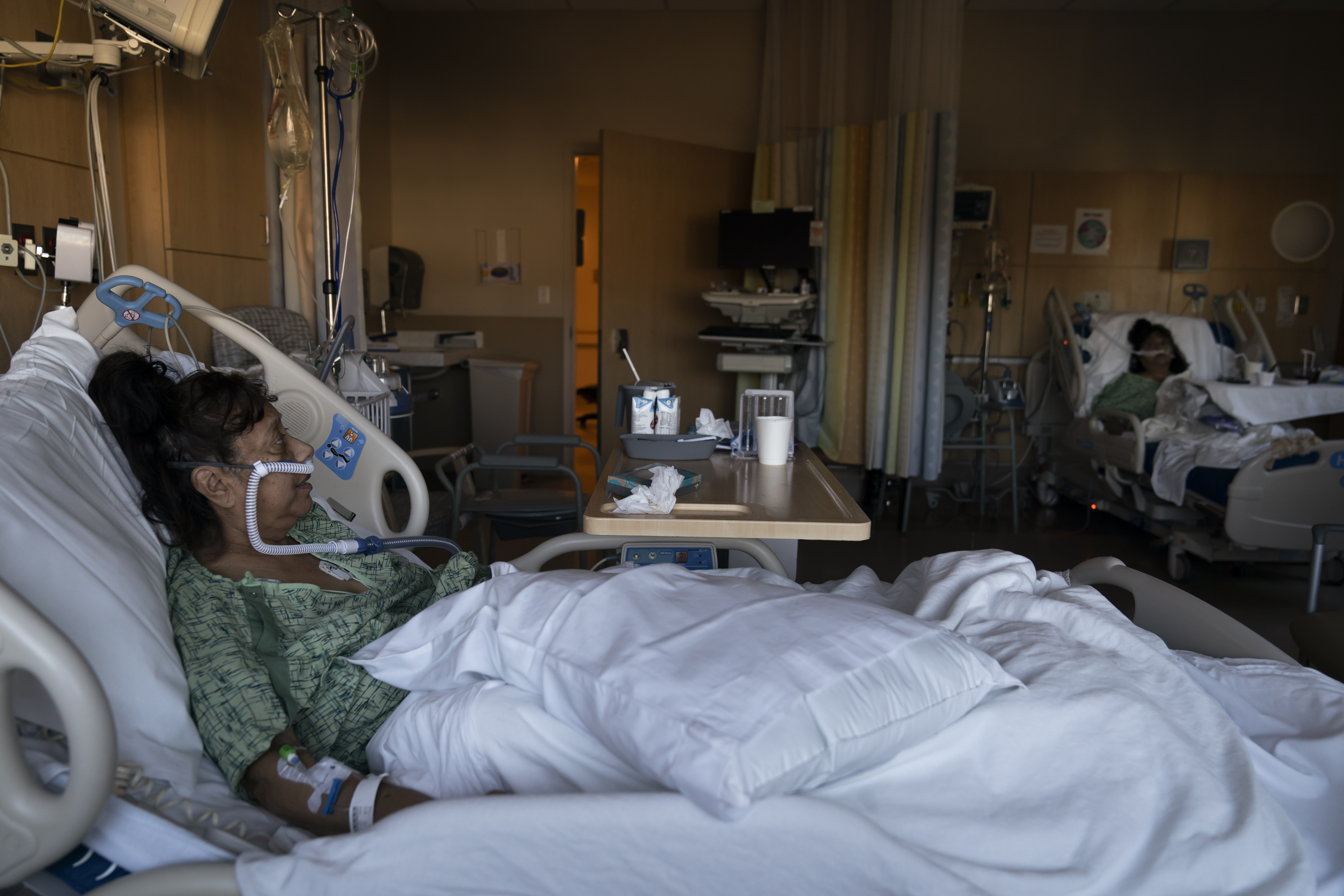 Natalie Balli, 71, and her twin sister, Linda Calderon, background right, watch TV as they rest in their beds in a COVID-19 unit at Providence Holy Cross Medical Center in Los Angeles, on Dec. 17. The sisters were admitted to the hospital on the same day, a few days after their Thanksgiving gathering. 