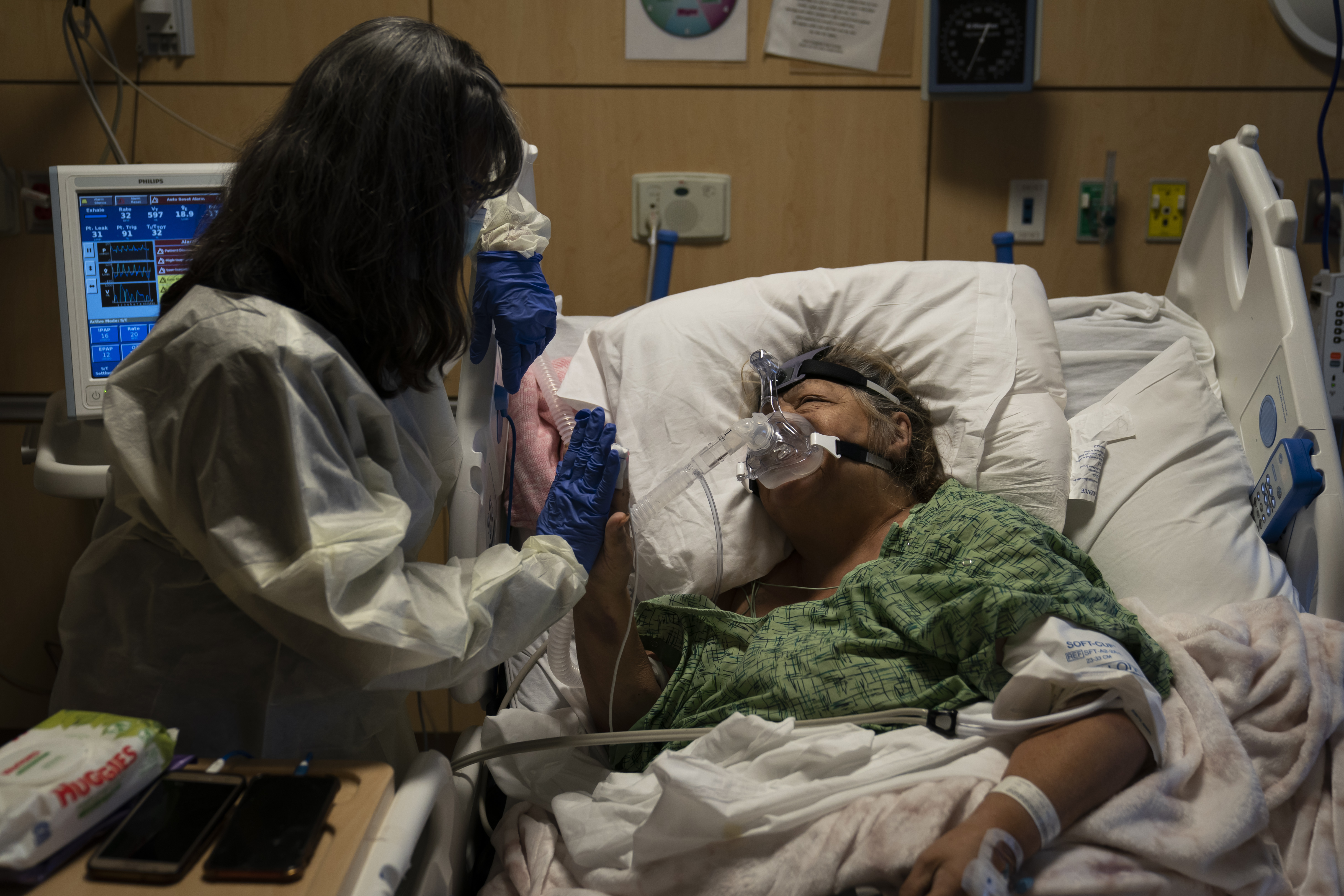 Becky Gonzalez, left, and her long-time friend, Mary Lou Samora, a 71-year-old COVID-19 patient, put their palms together after they shared some encouraging words at Providence Holy Cross Medical Center in Los Angeles, on Dec. 17.