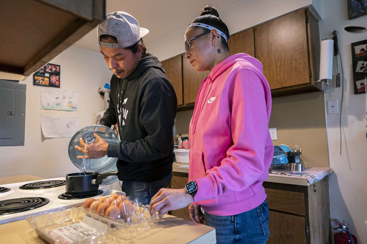 Erland Suppah Jr., left, and CeCelia LeClaire use donated water to cook lunch in their home on Tuesday, Dec. 7, 2021, in Warm Springs, Ore. The massive infrastructure bill signed earlier this year promises to bring change to some Native American tribes that lack clean water or indoor plumbing through the largest single infusion of money into Indian Country.