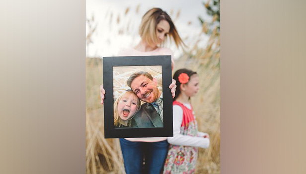 Alyssa Winslow and her daughter Kaya are pictured in the background as Alyssa holds a photo of her late husband, Ryan Chambers, and daughter Evee in the foreground. Alyssa recently published a memoir called "After the Victory," which shares the story of how she was able to continue on after Ryan and Evee were killed in a 2015 car crash.