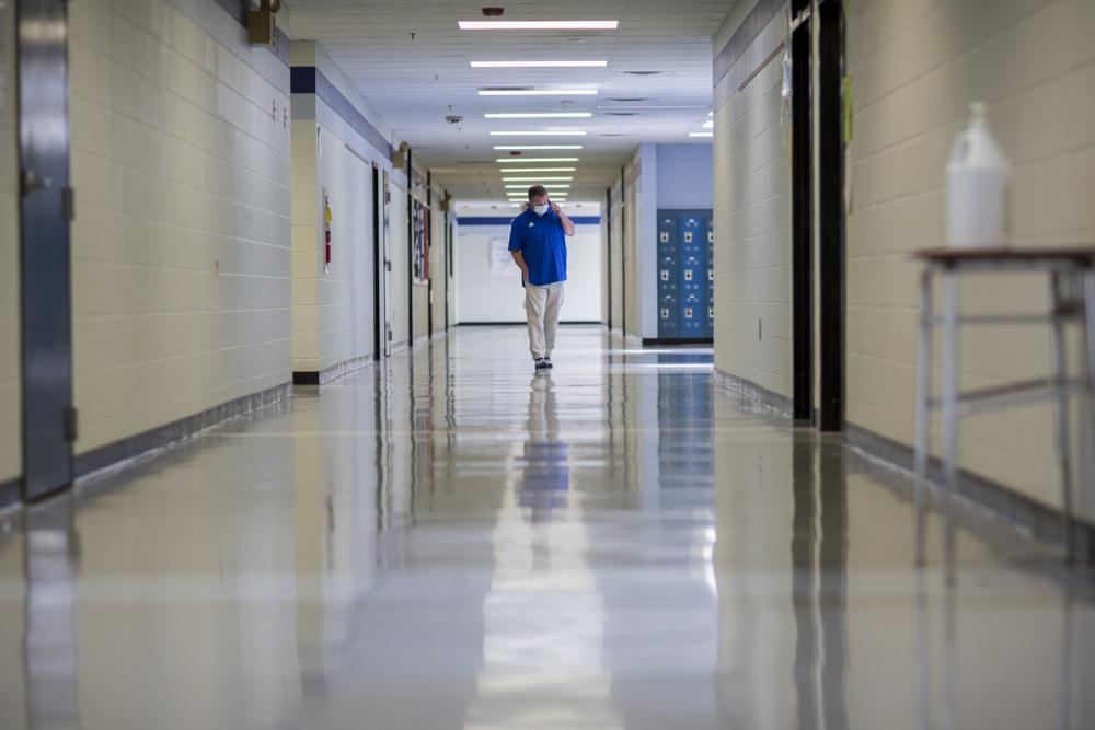 A middle school principal walks the empty halls of his school as he speaks with one of his teachers to get an update on her COVID-19 symptoms, Aug., 20, in Wrightsville, Ga.