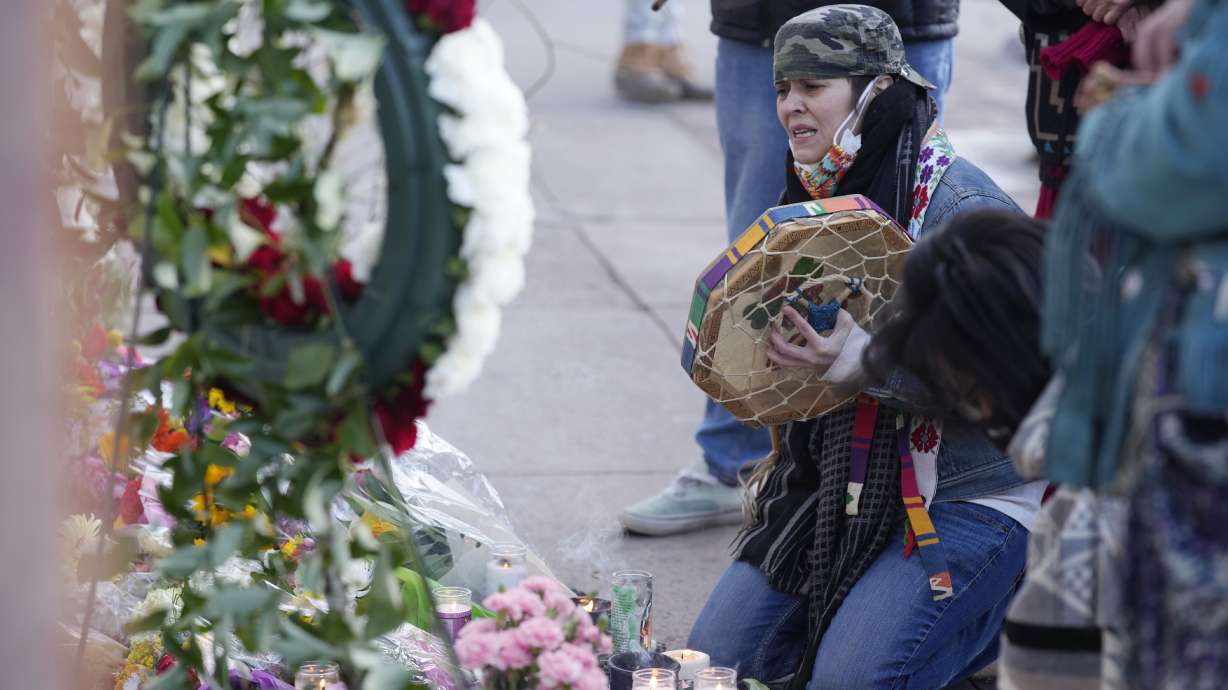 Mourners gather outside a tattoo parlor Tuesday in Denver, one of the scenes of a shooting spree that left multiple people dead. The suspect is believed to have written fictional books that described similar attacks.