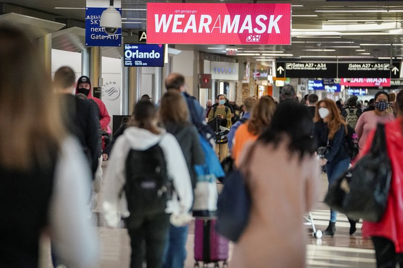 Travelers are seen under a PSA advising mask-wearing in a concourse during the holiday season as the coronavirus omicron variant threatens to increase case numbers at Hartsfield-Jackson Atlanta International Airport in Atlanta, Ga. on Dec. 22. Thousands of flights were delayed or canceled Friday in the U.S. and internationally.
