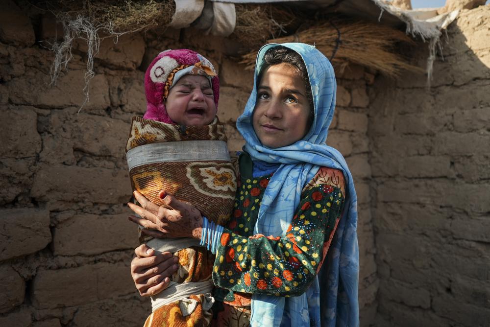 Qandi Gul holds her brother outside their home housing those displaced by war and drought near Herat, Afghanistan. Dec. 16. 