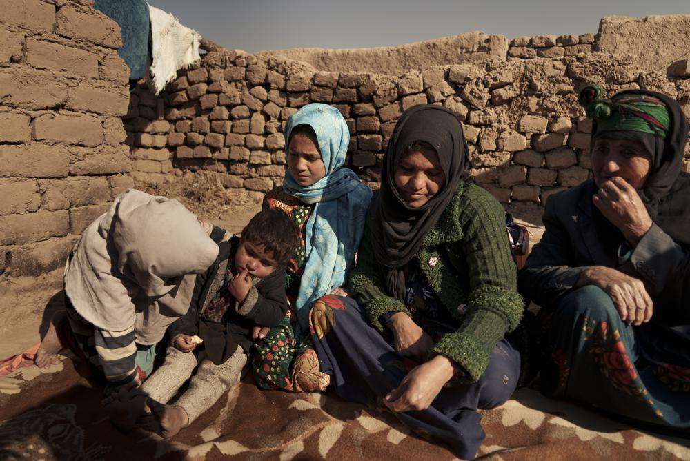 Aziz Gul, second from right, and her 10-year-old daughter Qandi, center, sit outside their home with other family members, near Herat, Afghanistan. Dec. 16.