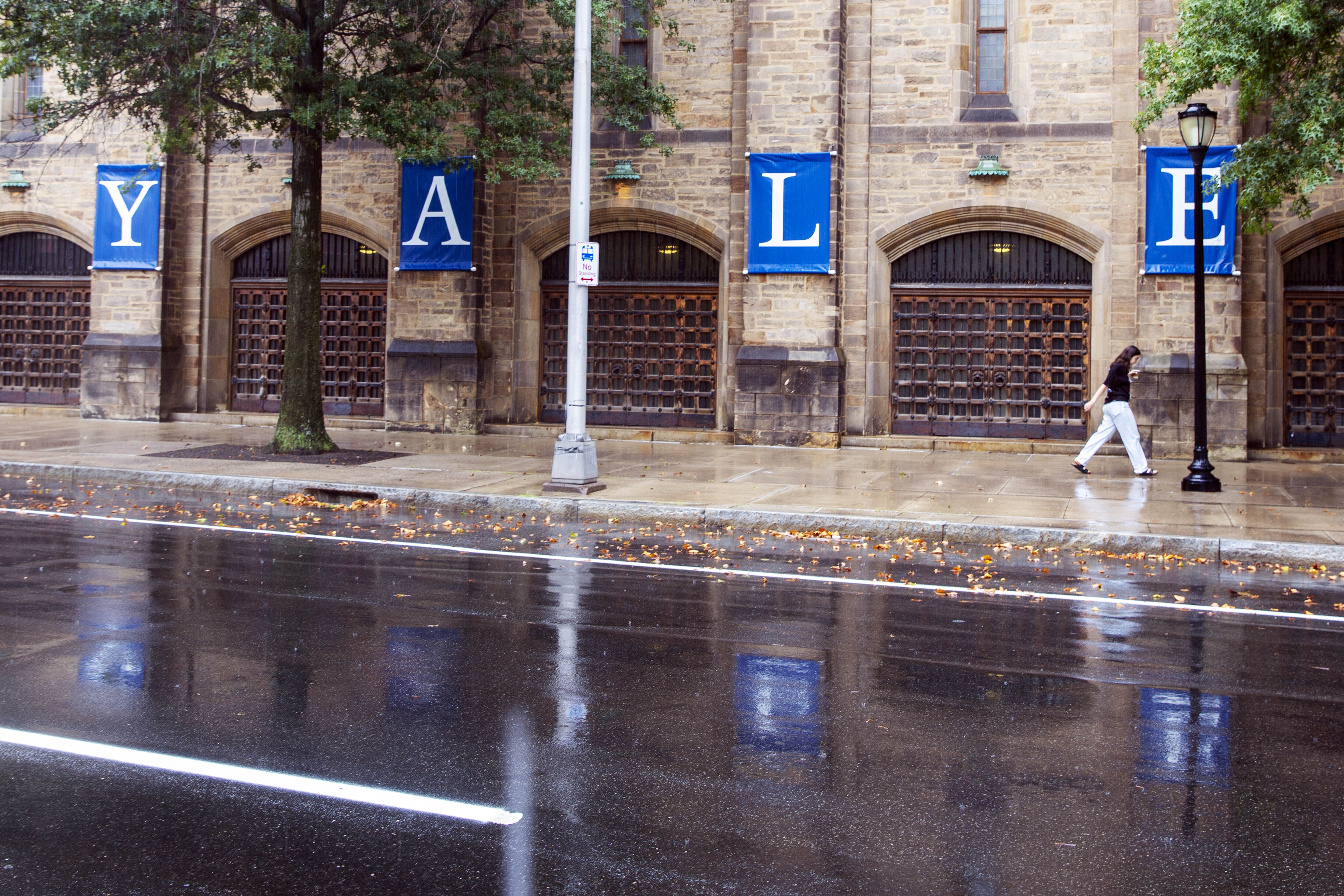 A woman walks by a Yale sign reflected in the rainwater in the street on the Yale University campus in New Haven, Connecticut on Aug. 22, 2021.