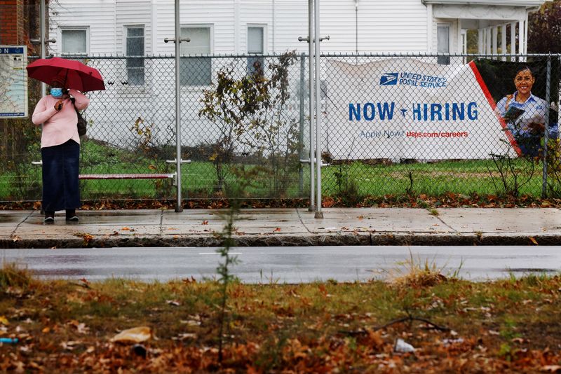 A woman waits for a bus next to a "Now Hiring" sign in Boston, Mass., Oct. 30, 2021. U.S. employment increased less than expected in December.