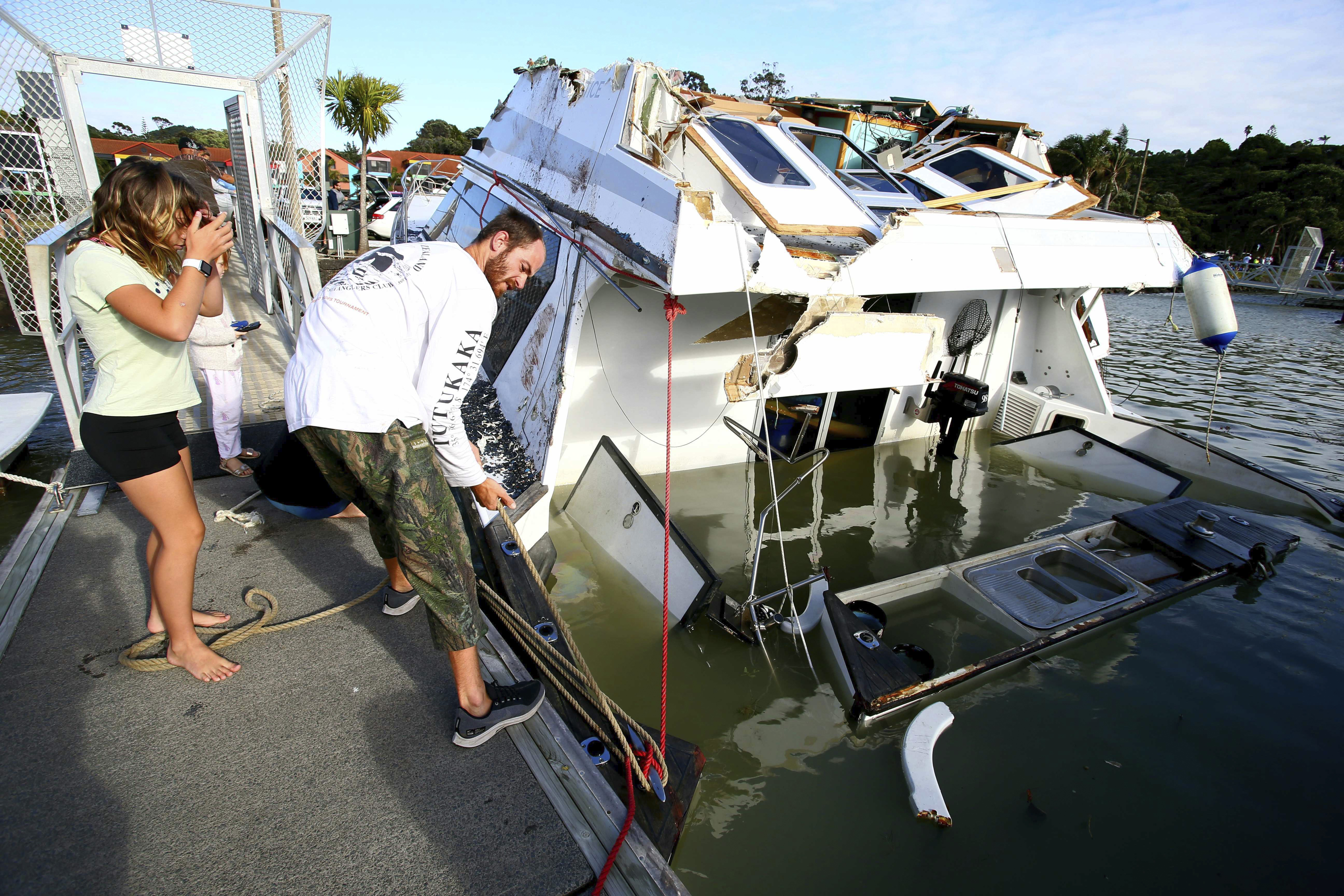 A couple look at a damaged boat in a marina at Tutukaka, New Zealand, Sunday, after waves from a volcano eruption swept into the marina.