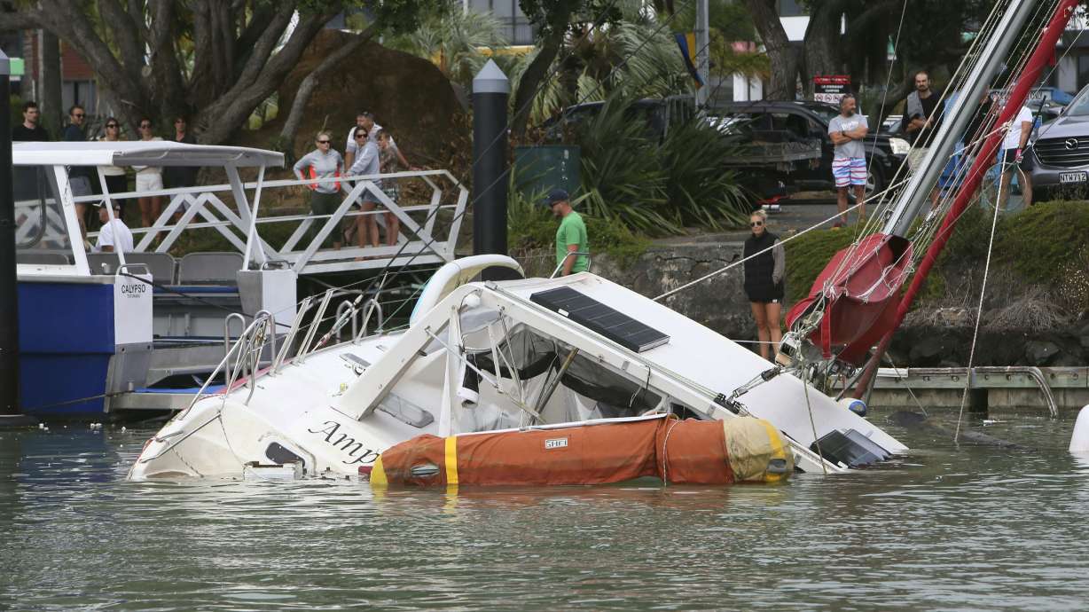People look at a damaged boat in a marina at Tutukaka, New Zealand, Sunday, after waves from a volcano eruption swept into the marina.