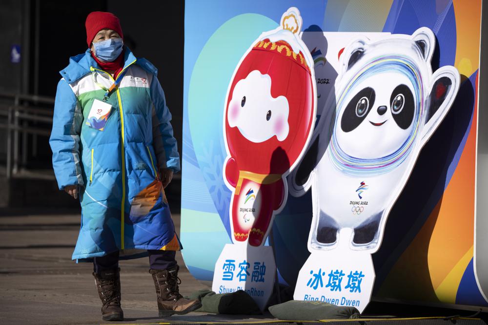 A woman wearing a face mask to protect against COVID-19 stands next to figures of the Winter Paralympic mascot Shuey Rhon Rhon left, and Winter Olympic mascot Bing Dwen Dwen on a pedestrian shopping street in Beijing, Saturday. 