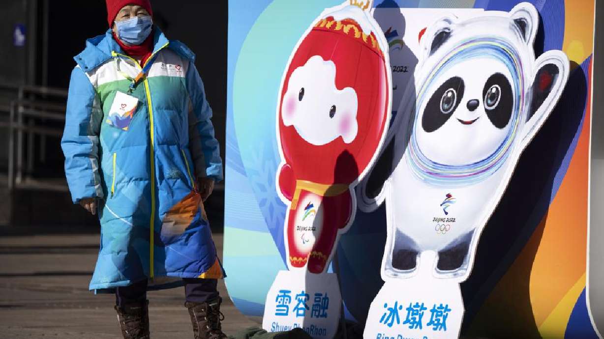 A woman wearing a face mask to protect against COVID-19 stands next to figures of the Winter Paralympic mascot Shuey Rhon Rhon left, and Winter Olympic mascot Bing Dwen Dwen on a pedestrian shopping street in Beijing, Saturday.