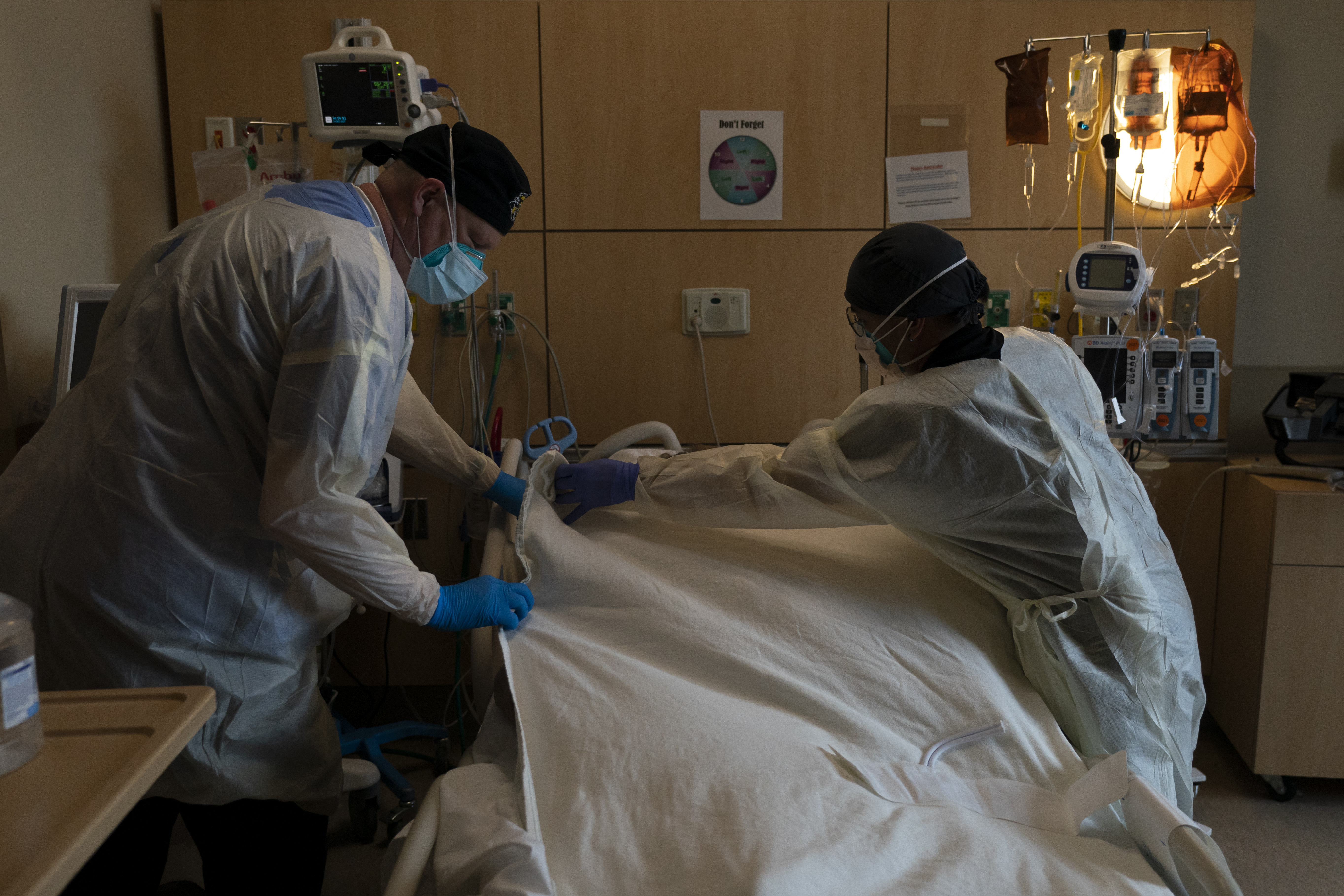 Respiratory therapist Frans Oudenaar, left, and registered nurse Bryan Hofilena cover a body of a COVID-19 patient in Los Angeles, Dec. 14, 2021. The fast-moving omicron variant may cause less severe disease on average, but COVID-19 deaths in the U.S. are climbing.