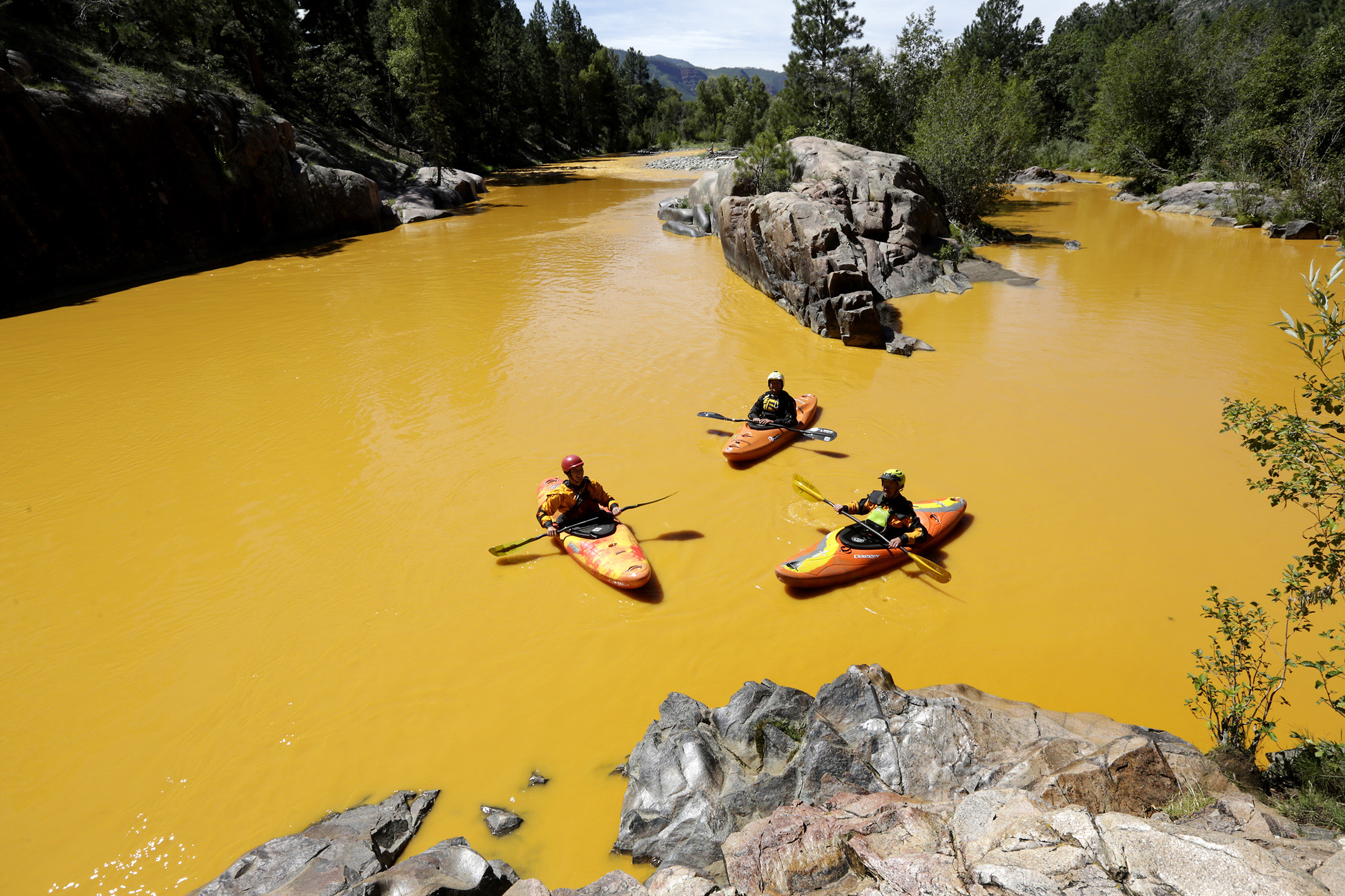 People kayak in water colored from a mine waste spill at the Animas River near Durango, Colo., on Aug. 6, 2015. Colorado, the U.S. government and a gold mining company have agreed to resolve a longstanding dispute over who's responsible for continuing cleanup from the spill.