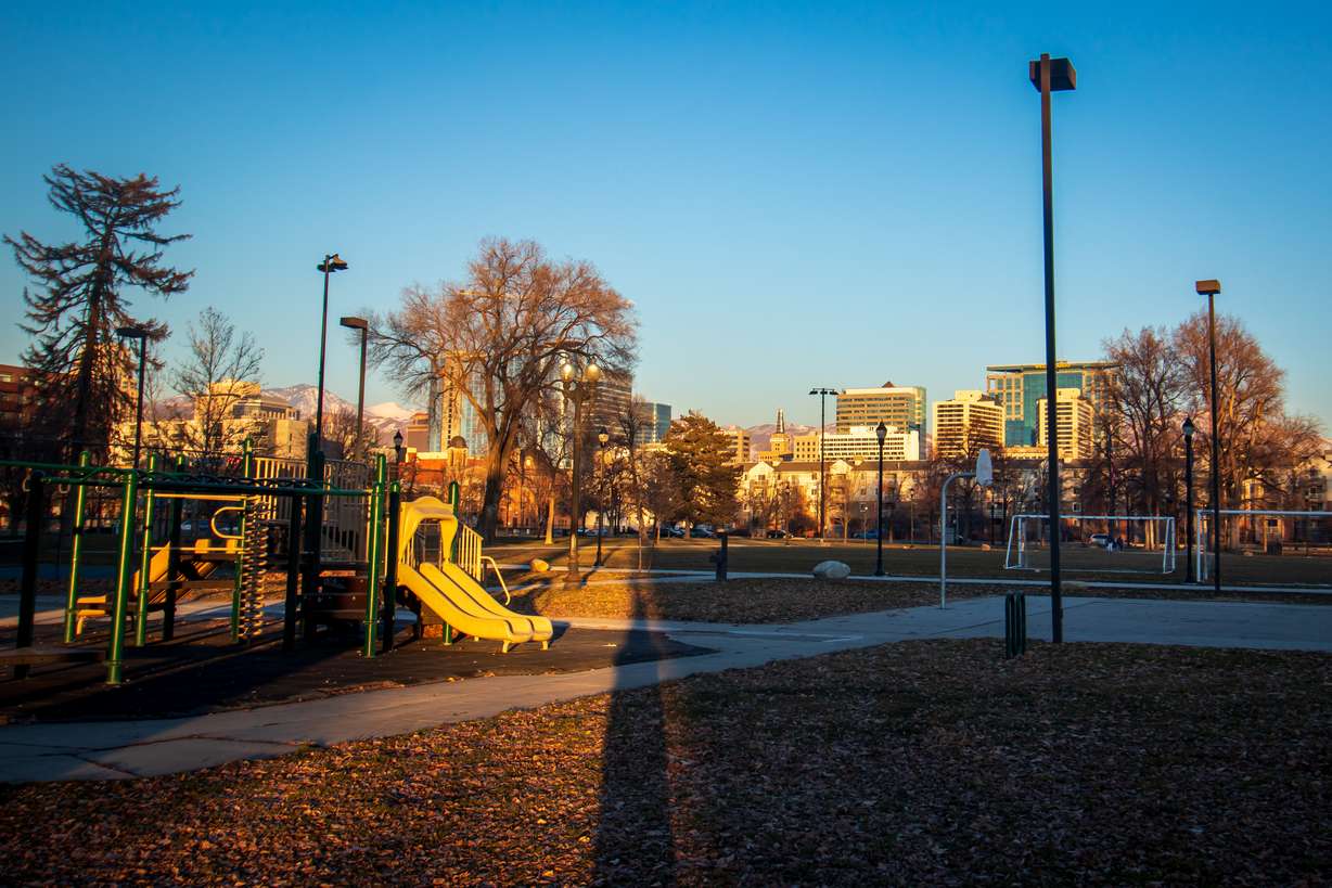 An empty playground and basketball court at Pioneer Park on Sunday evening. The city's downtown buildings can be seen in the background.