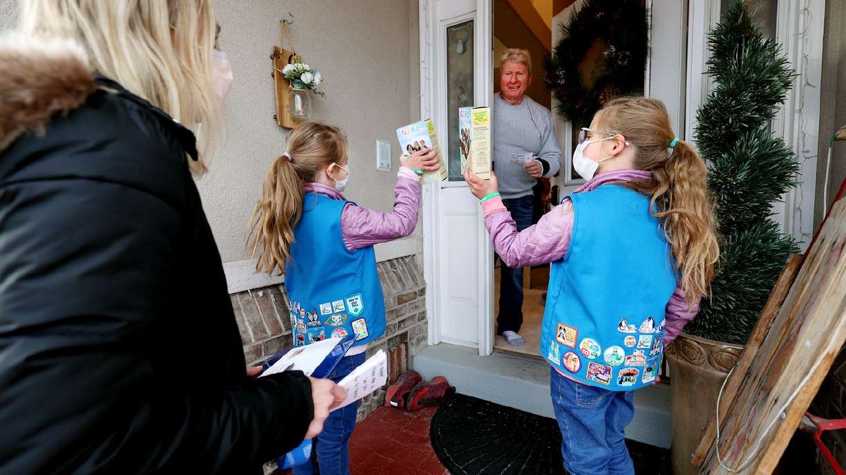 Steve Weller listens to Annie and Juliet Agy talk about the different cookies as their mother Kalie Agy watches as they go door to door selling Girl Scout Cookies in Cottonwood Heights on Tuesday.
