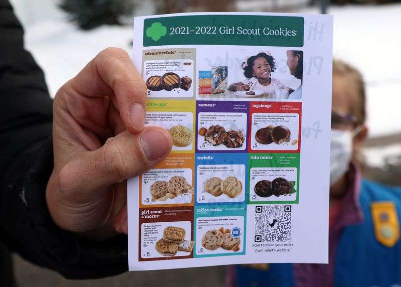 Kalie Agy shows a flyer she had printed to help people make their selections as she and her daughters Juliet and Annie go door-to-door selling Girl Scout Cookies in Cottonwood Heights on Tuesday.